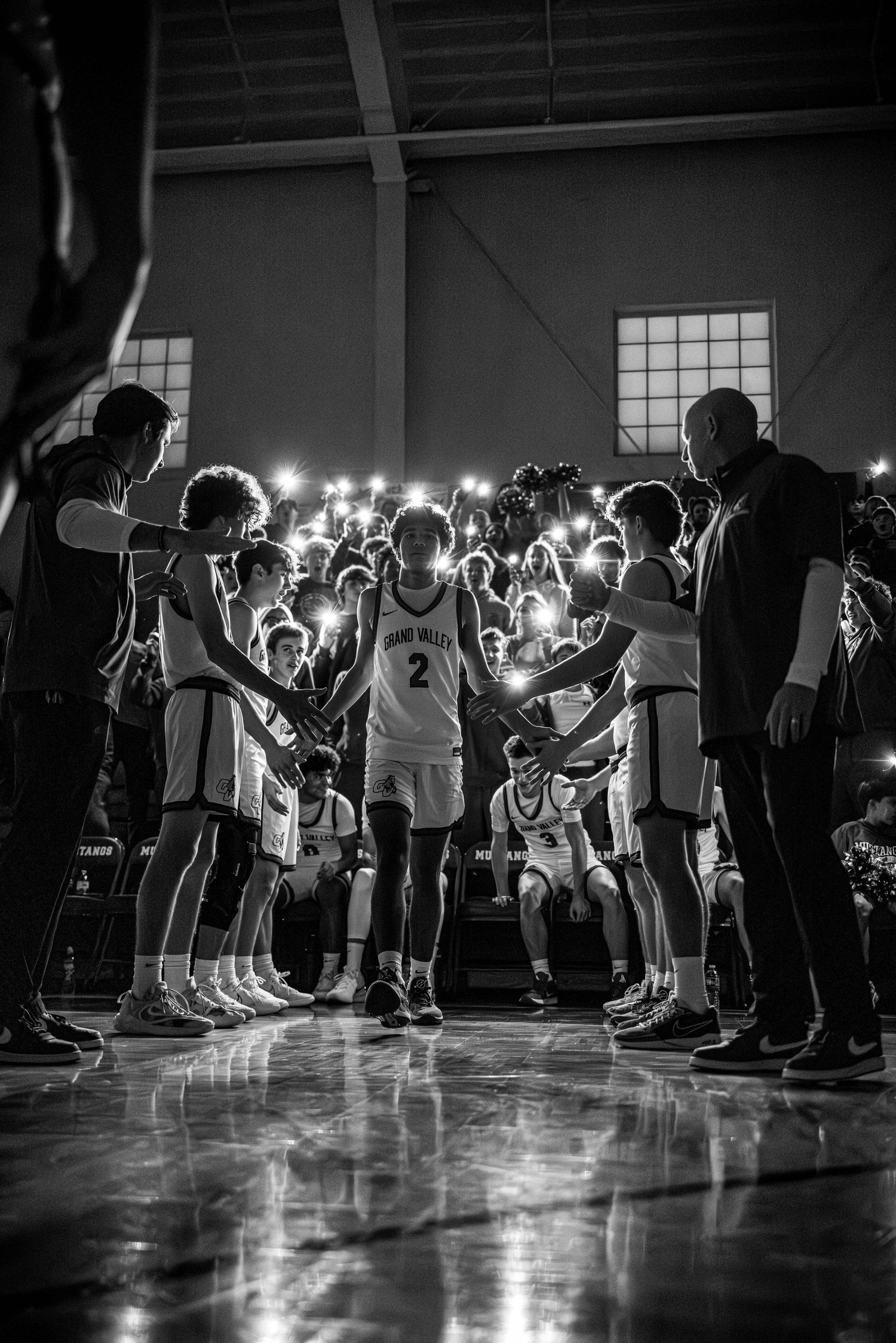 Basketball player number 2 walks through teammate tunnel with sparklers in dramatic black and white arena photograph.