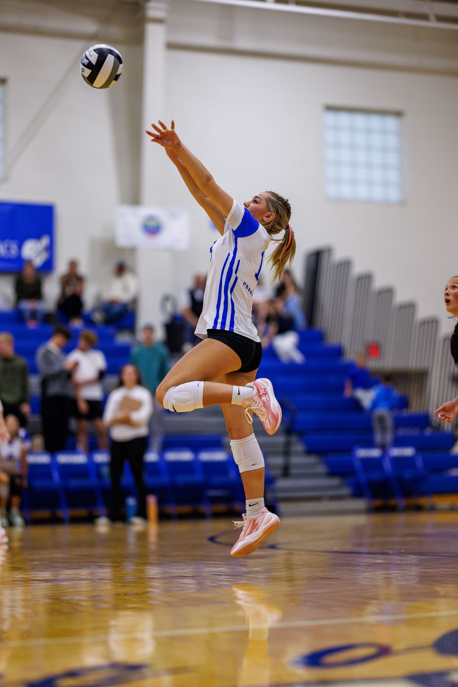 Female volleyball player leaps high to spike the ball during a competitive indoor gymnasium match.