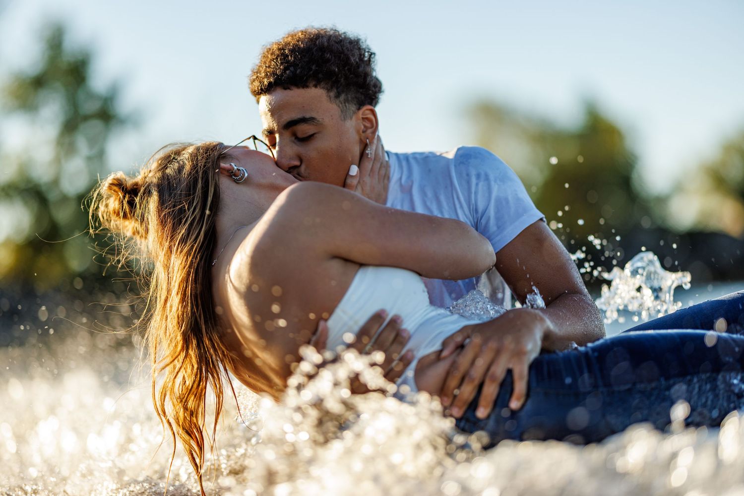 A couple sharing a passionate kiss while splashing in sun-drenched water in a golden outdoor setting.