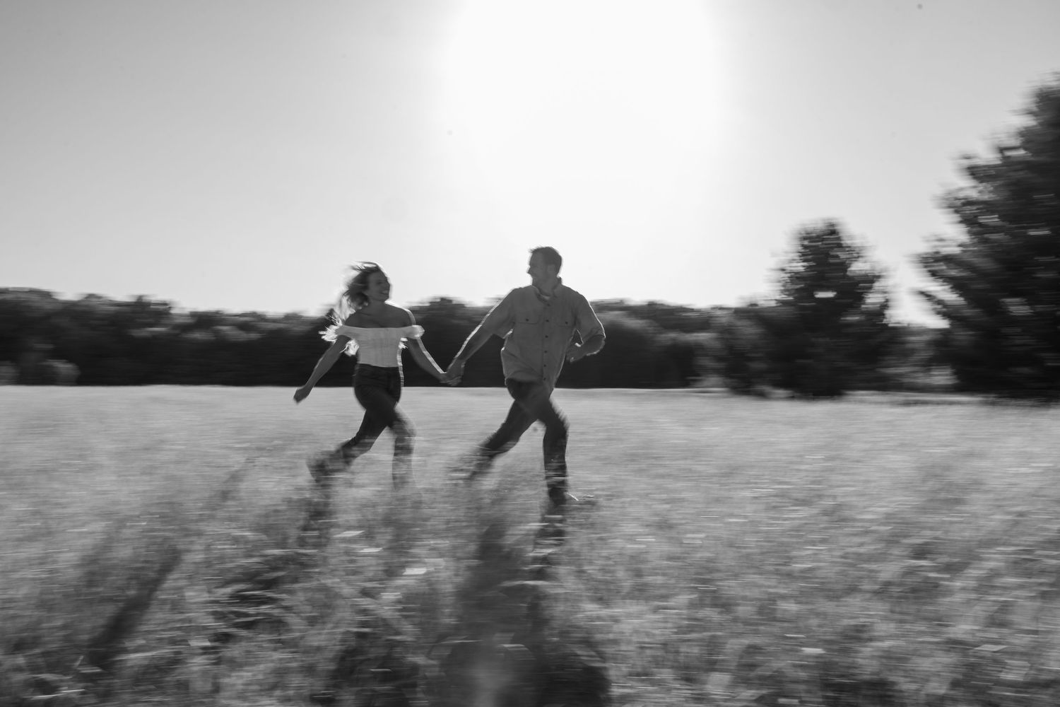 Two children run through a sunlit field holding hands in a blurred black and white photo.