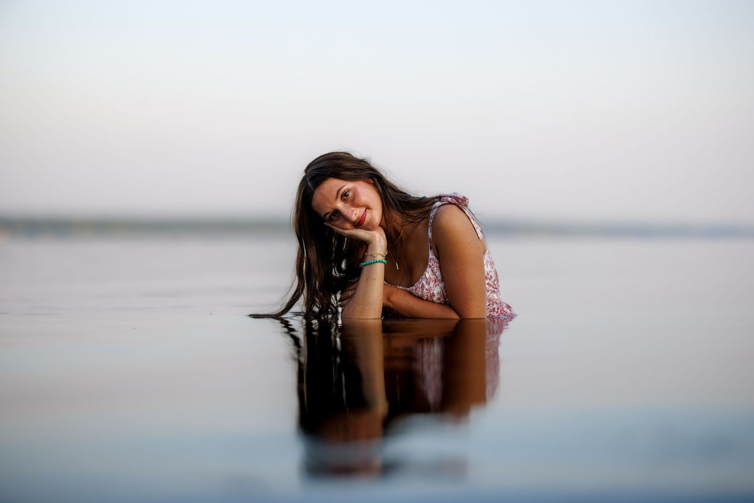 Young woman lying in shallow water with reflection visible on calm lake surface.