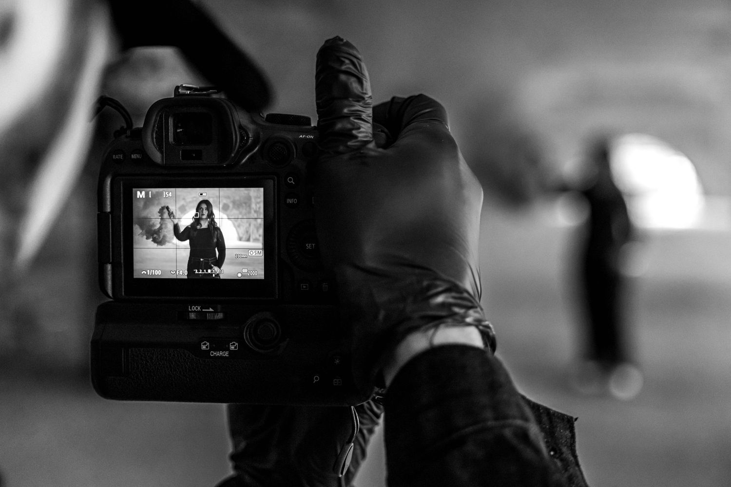 Photographer captures woman through camera viewfinder in black and white behind-the-scenes shot.