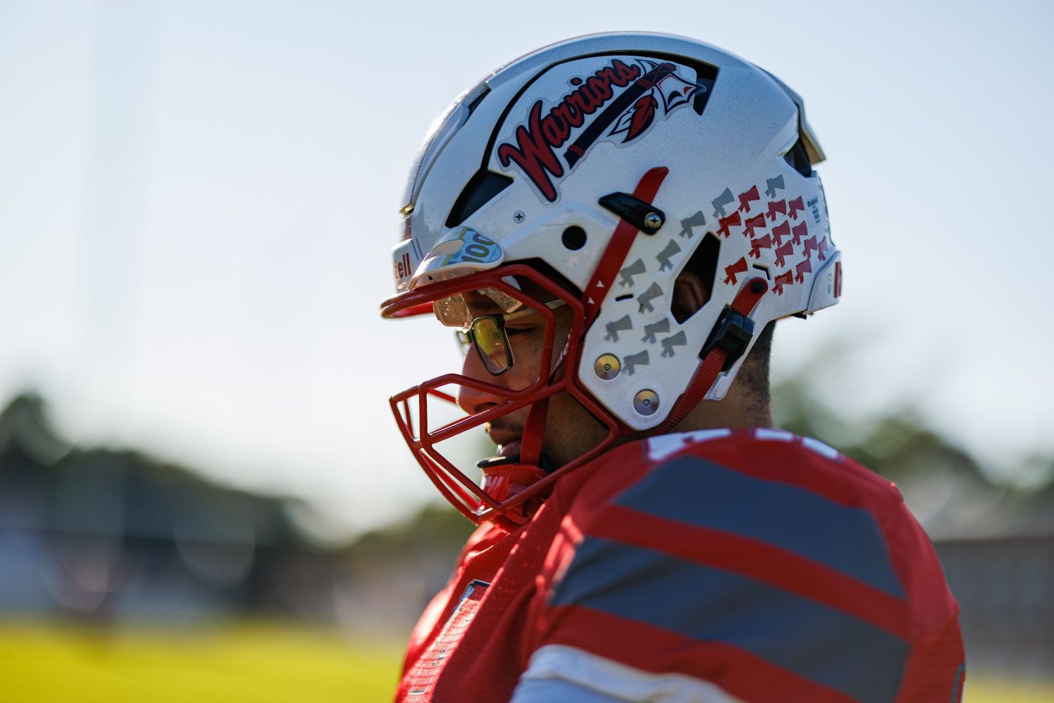 Close-up profile of football player wearing white Warriors helmet with stickers in outdoor stadium setting.