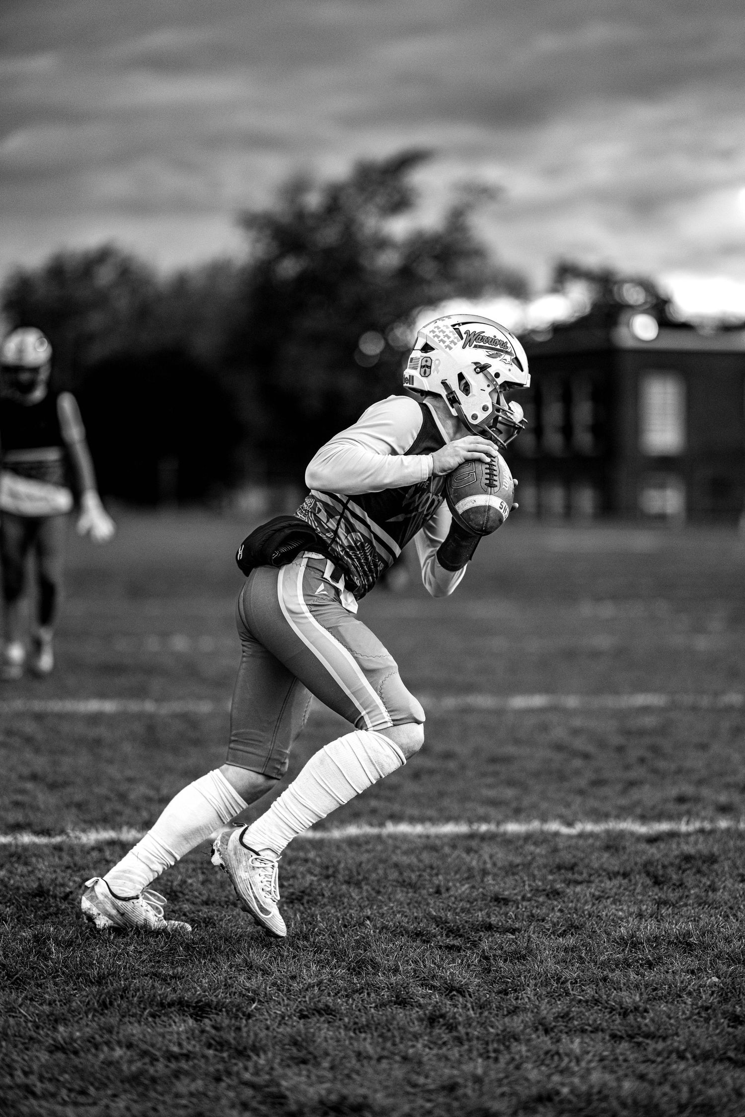 A football player in black and white photo catches the ball during a game on a cloudy day.
