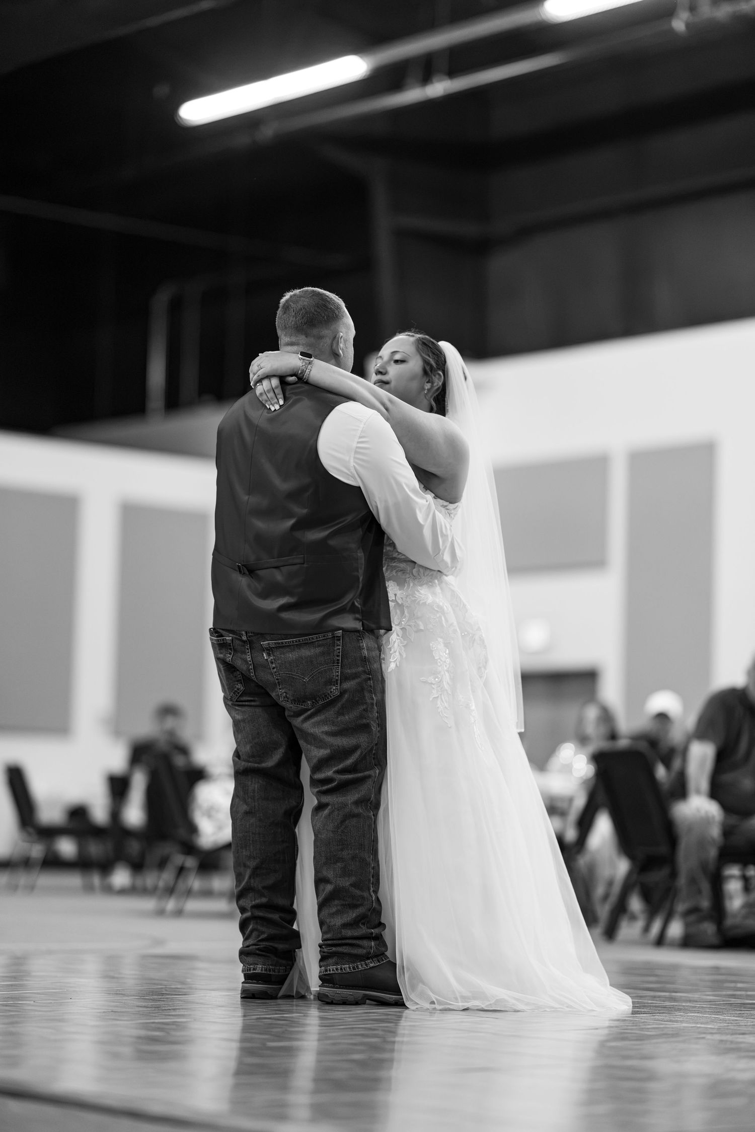 Bride and groom sharing first dance embracing on dance floor in black and white.