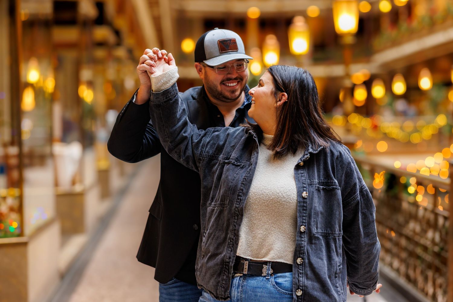 A happy couple dances together indoors surrounded by warm glowing lights in a decorated hall.
