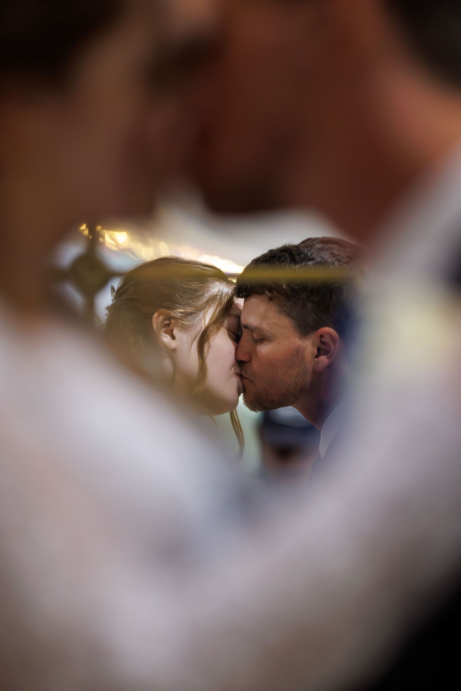 Bride and groom sharing an intimate kiss captured through a soft bokeh frame of surrounding guests.