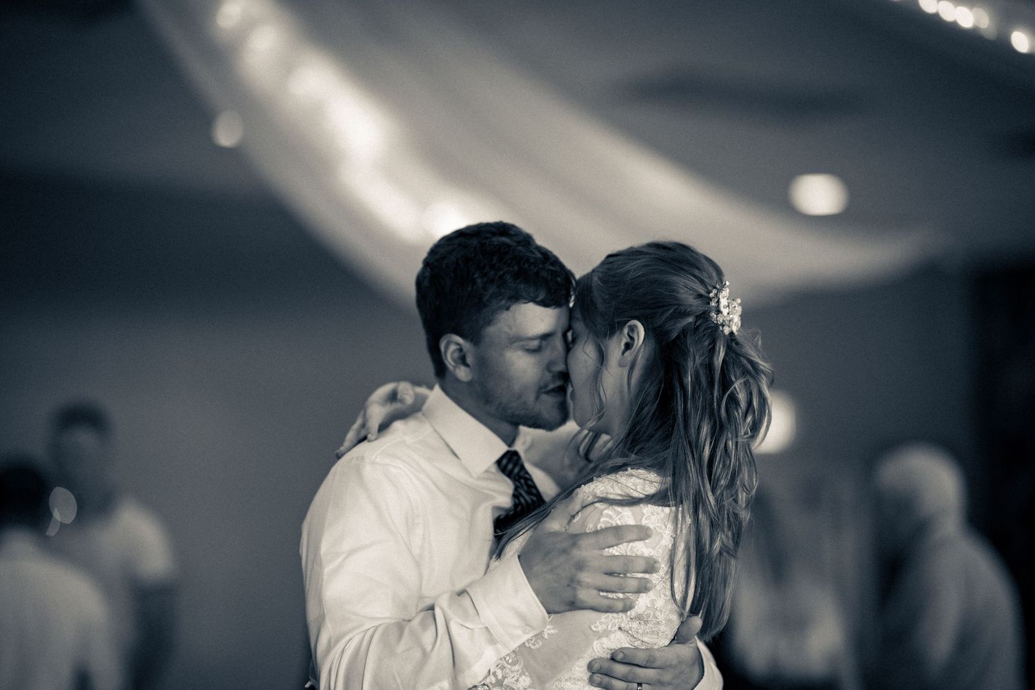 A couple shares a passionate first dance kiss in black and white under draped fabric at their wedding reception.