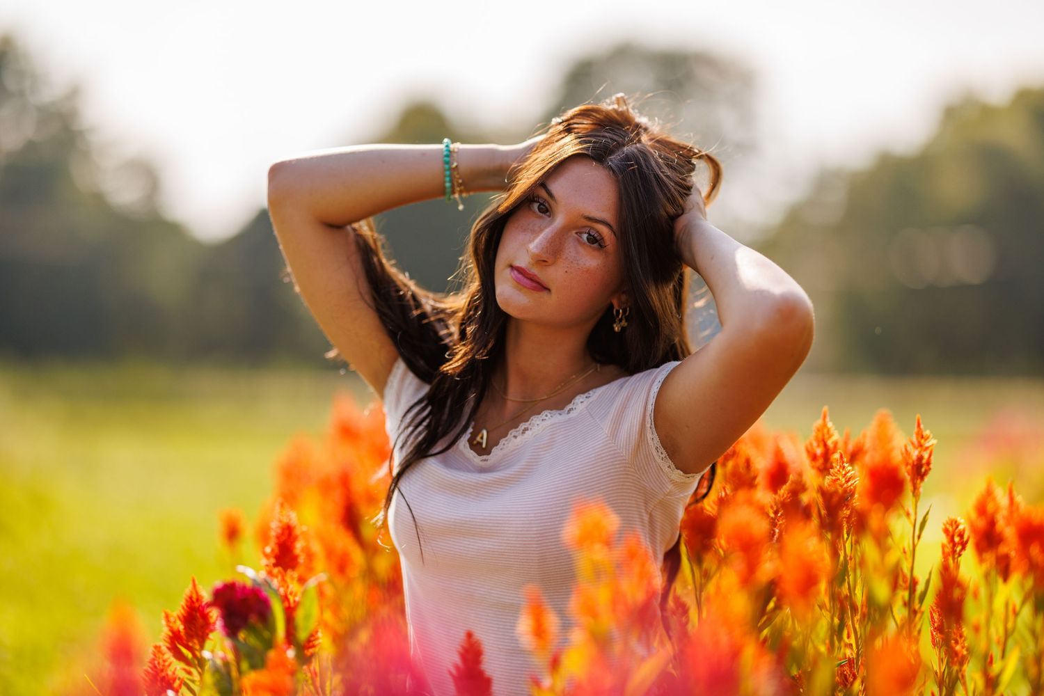 Young woman with long dark hair posing with hands raised in a field of bright red and orange flowers.