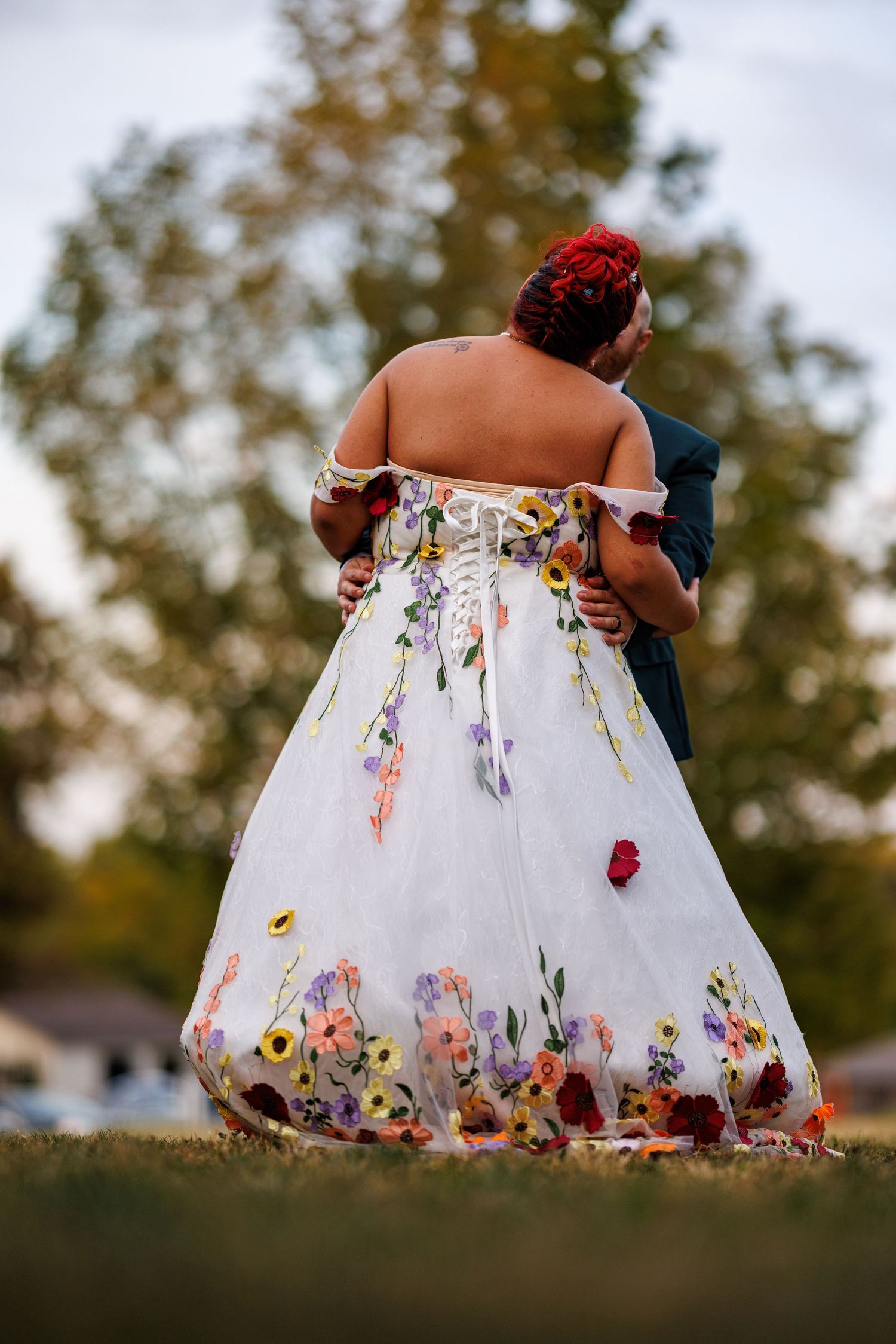Couple embracing outdoors, bride wearing stunning white floral wedding dress with painted wildflowers.