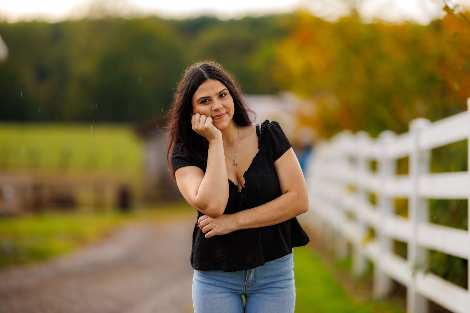 Smiling young woman in black top and jeans standing on rural farm path.