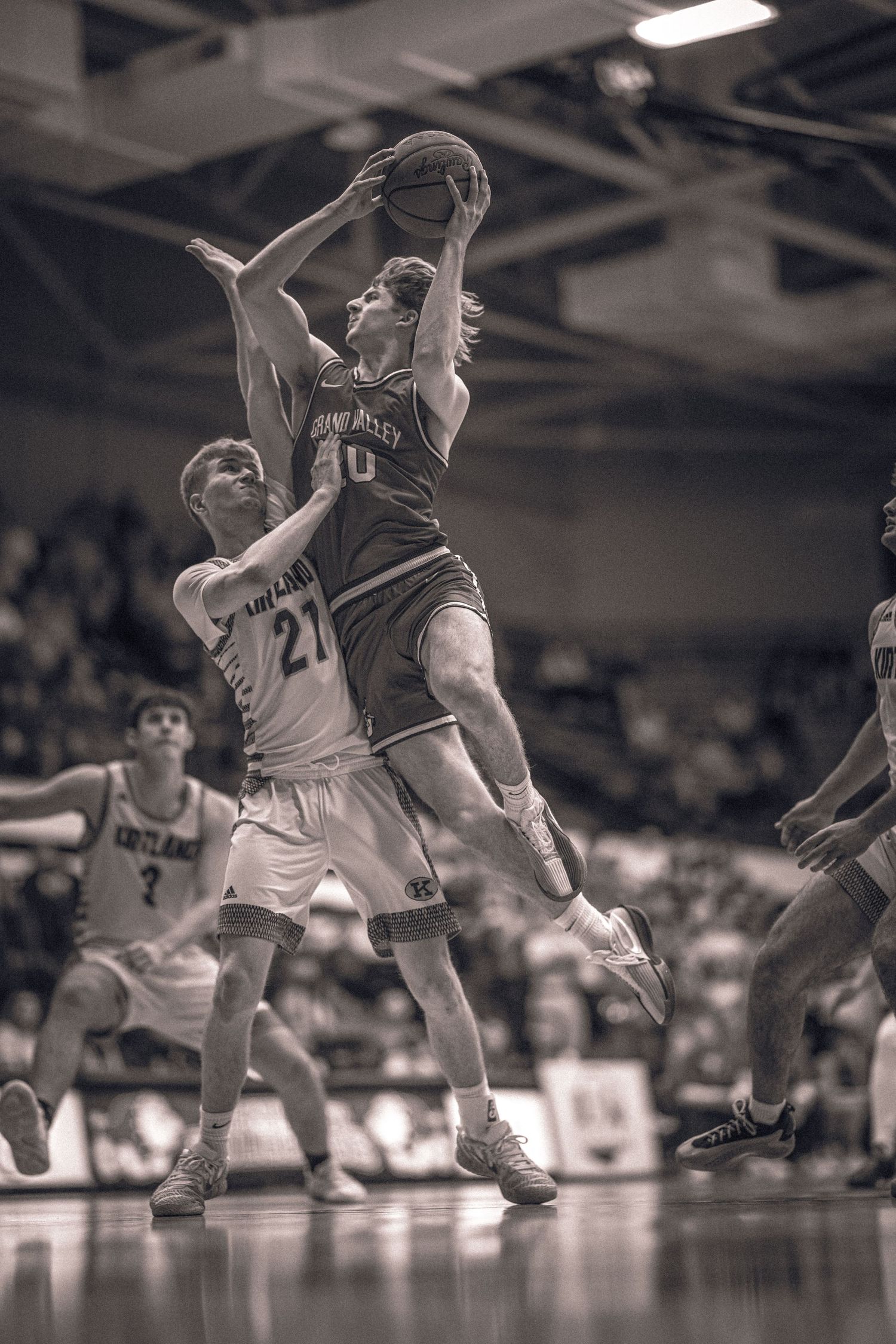 Basketball player leaping for a layup against a defender in a packed arena.