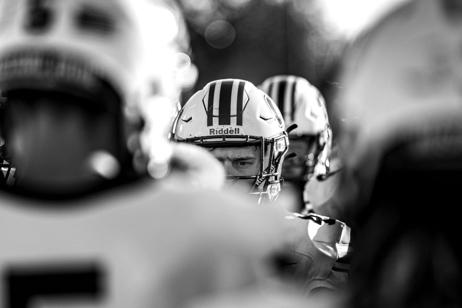 Black and white close-up of focused football players huddled together wearing helmets before a game.