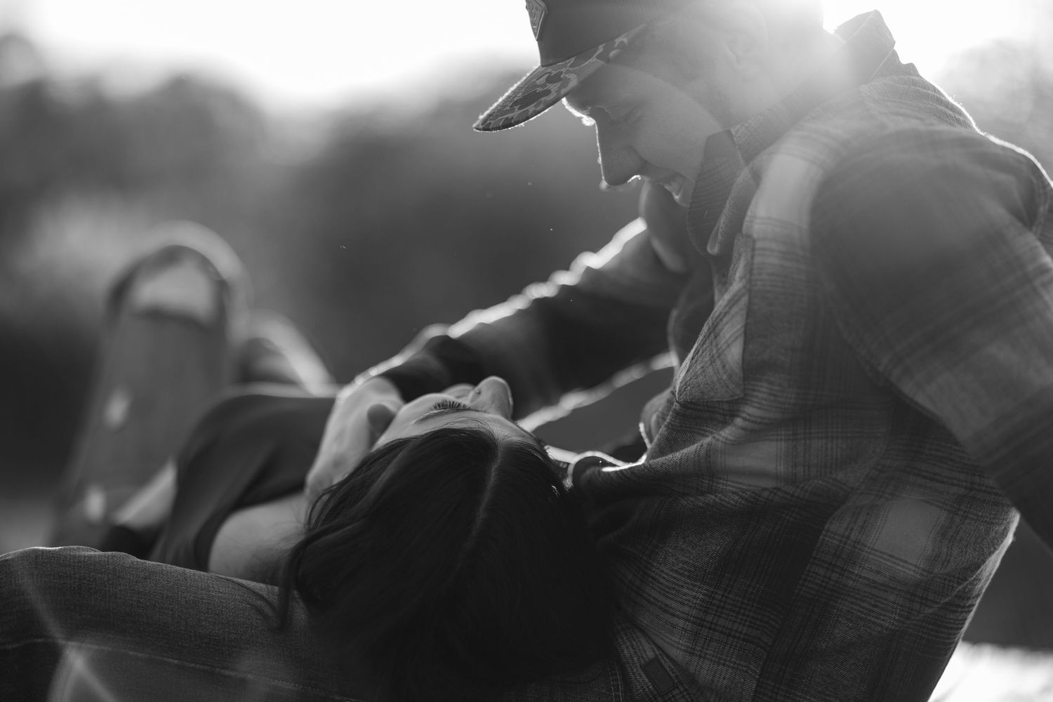 Black and white photo of couple sharing intimate moment in soft backlit setting.