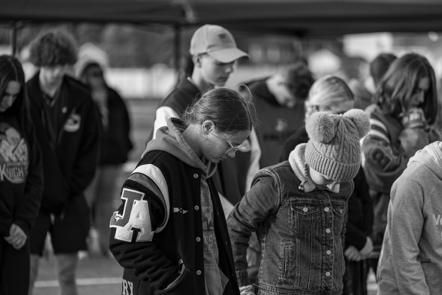 Young people bow their heads in prayer at an outdoor Christian youth gathering.
