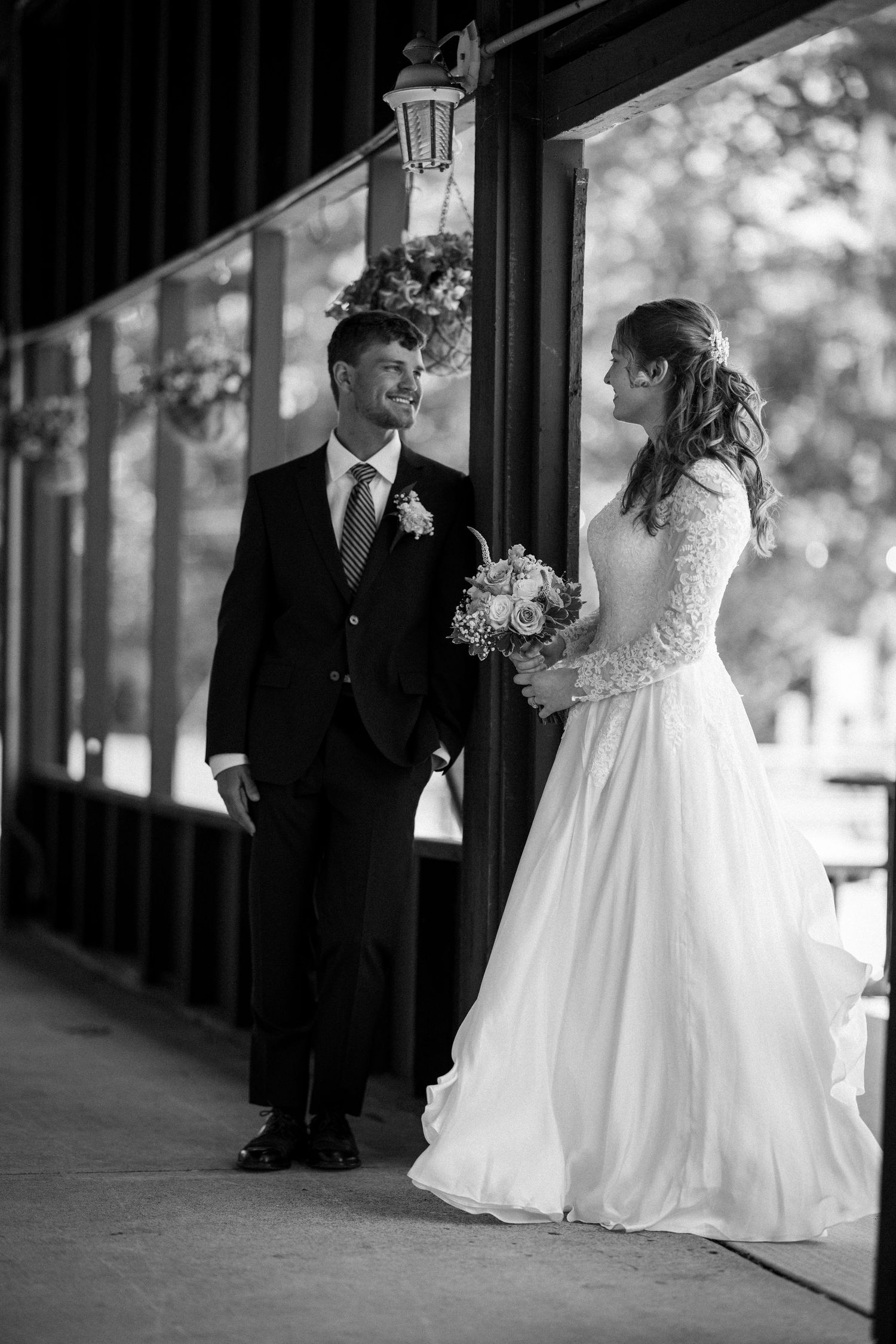 Bride holding bouquet and groom in suit sharing a romantic moment on a venue porch in black and white.