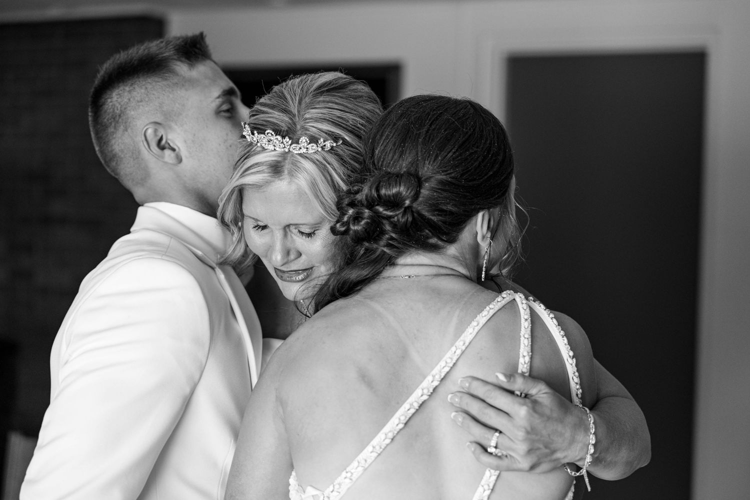 Emotional group hug between bride and two guests at wedding in black and white.