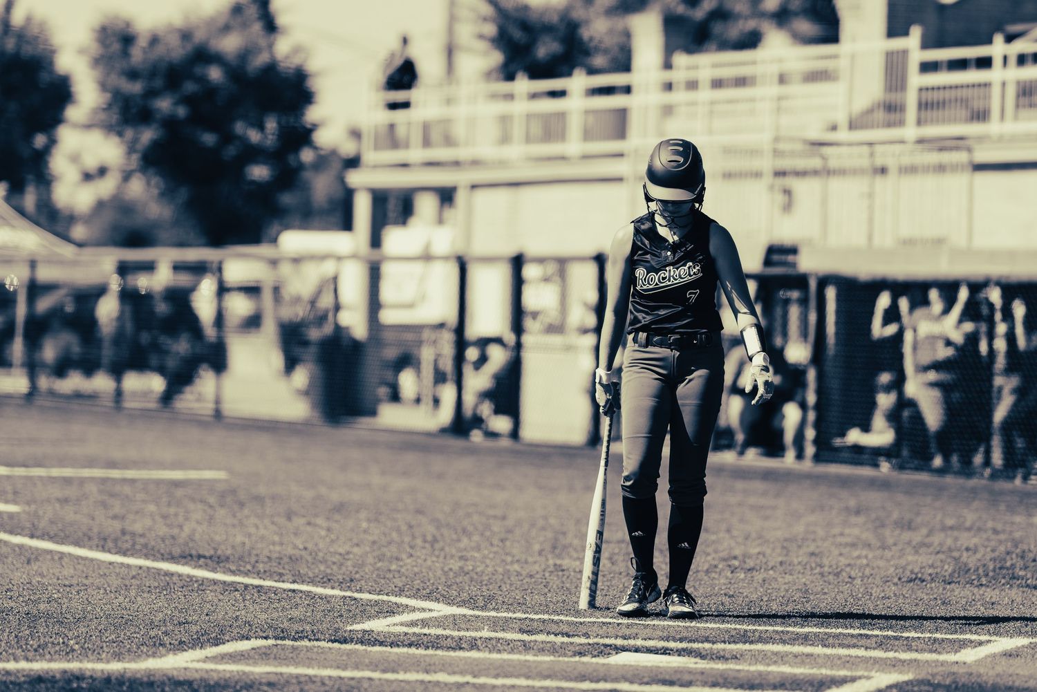 A softball batter stands at home plate holding bat in a vintage black and white toned photograph.