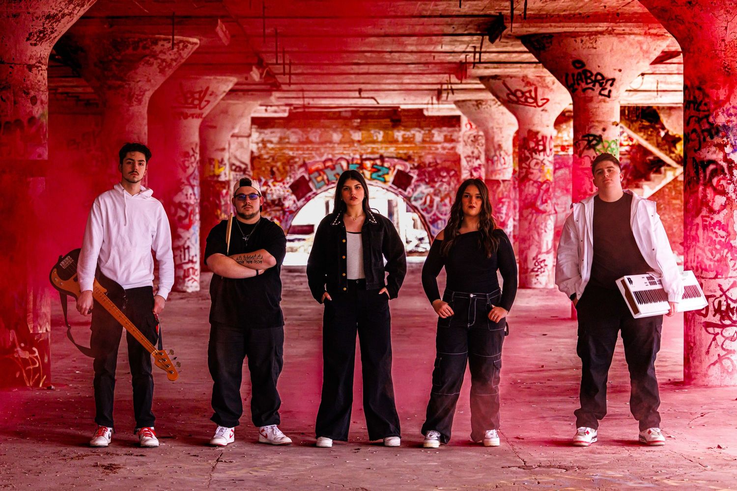 Five musicians pose in a graffiti-covered tunnel bathed in red light.