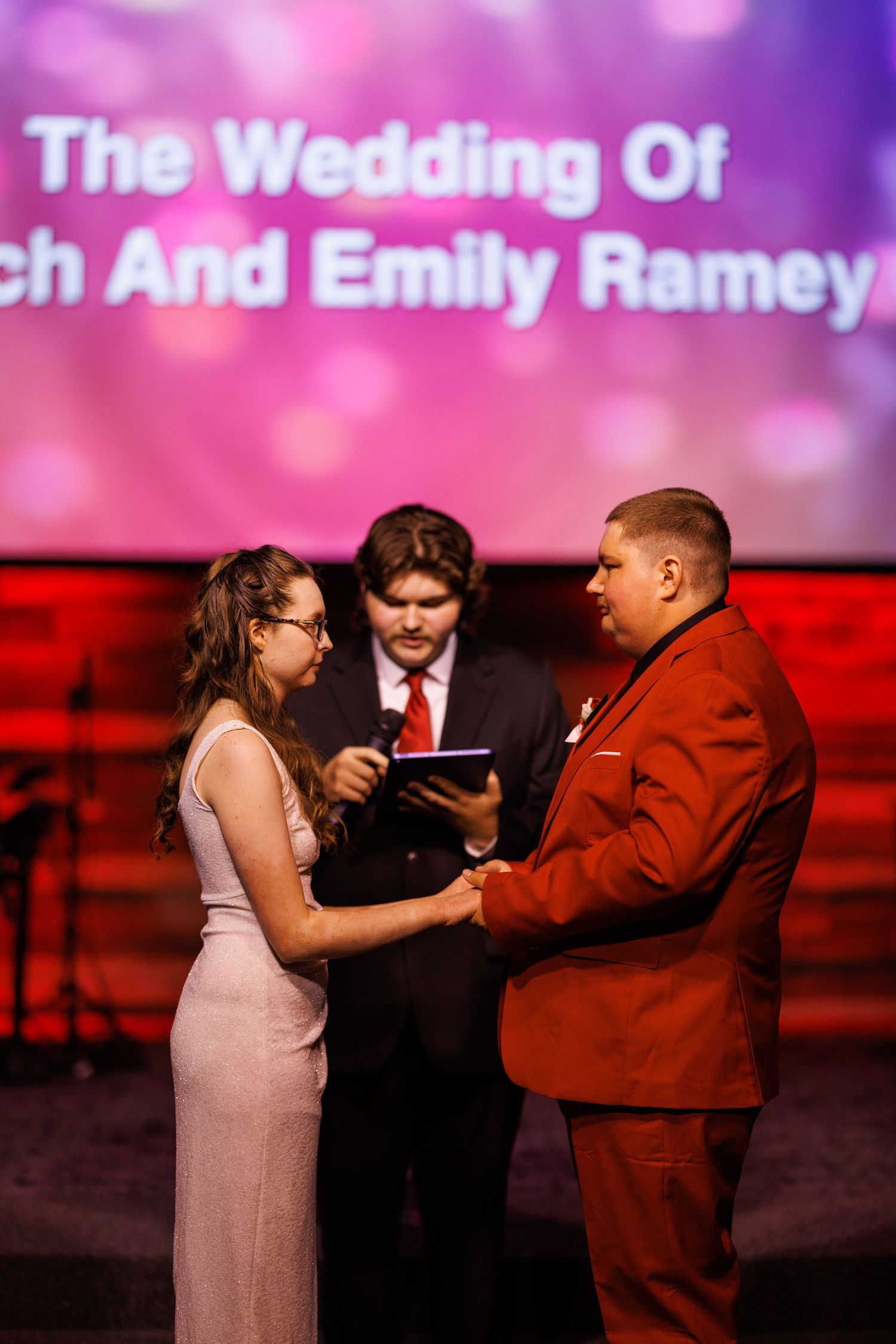 Bride and groom exchanging vows at altar with officiant during church wedding ceremony on stage.