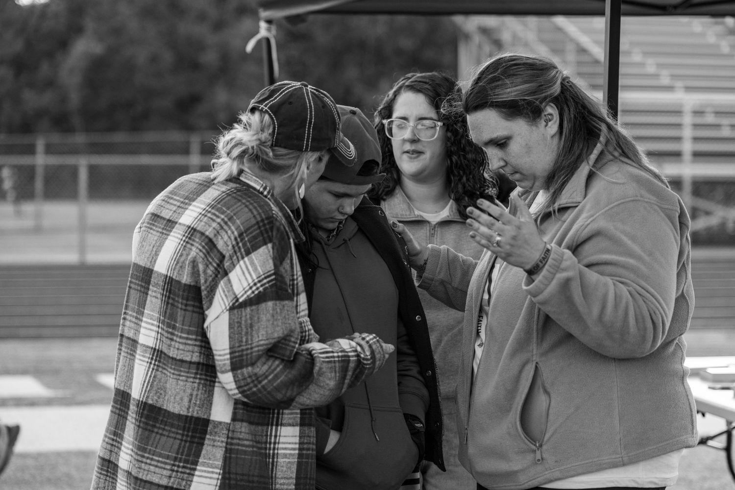 Three people bow their heads together in prayer at an outdoor Christian gathering.