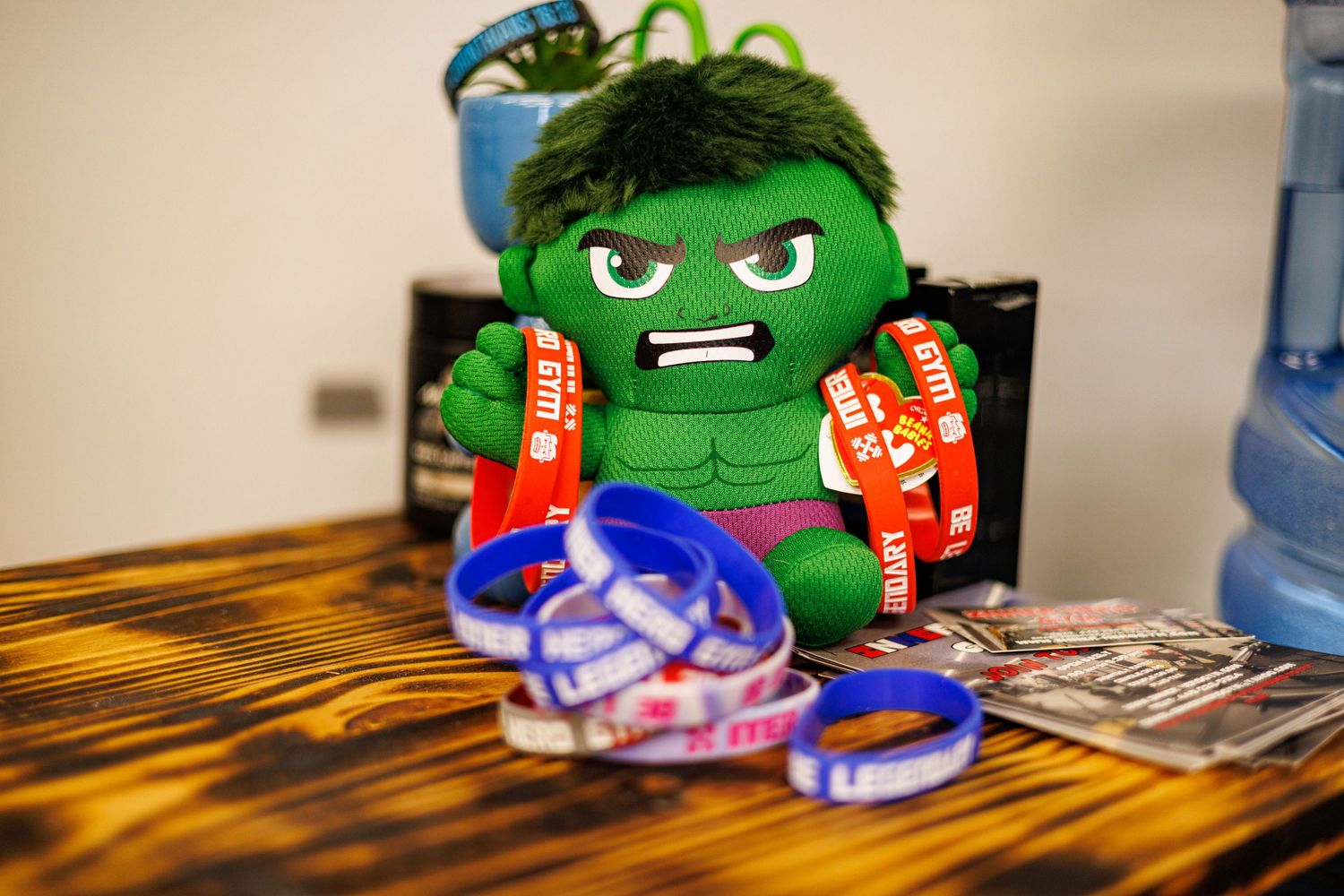 Hulk plush toy displayed with red and blue promotional wristbands and cards on wooden table.