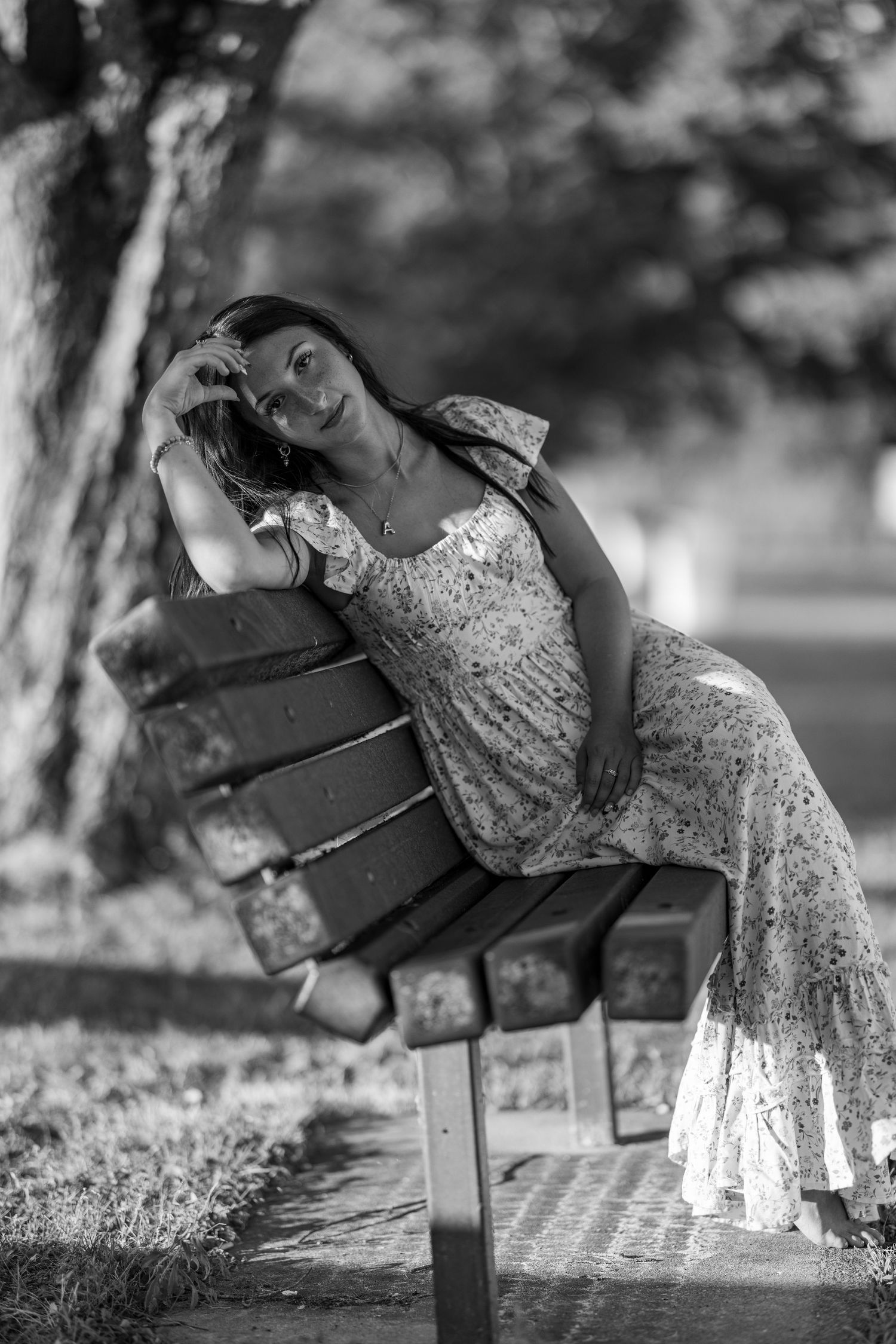 Woman in floral dress posing on wooden park bench in black and white photo.