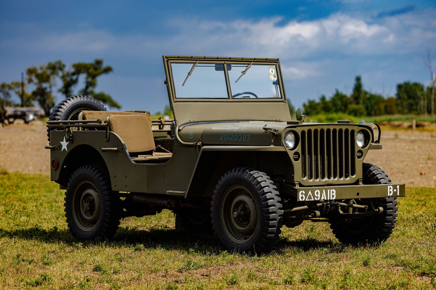 Vintage WWII military Willys Jeep in olive green parked on grass field at outdoor reenactment event.