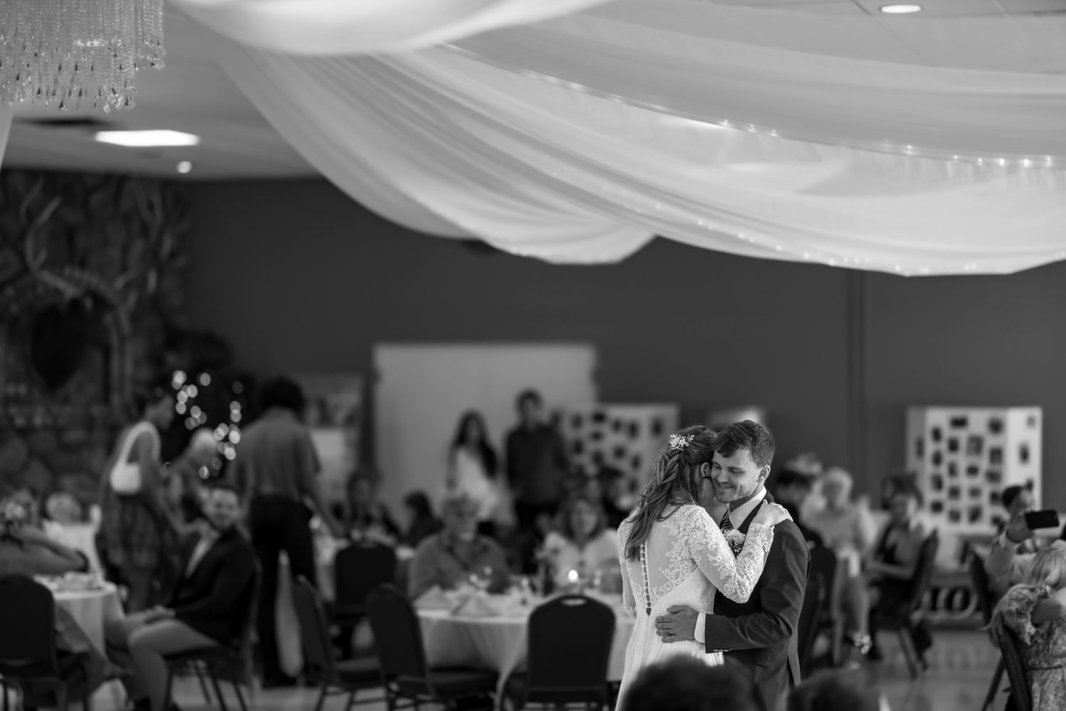 A couple shares their first dance at a wedding reception in a black and white photo.