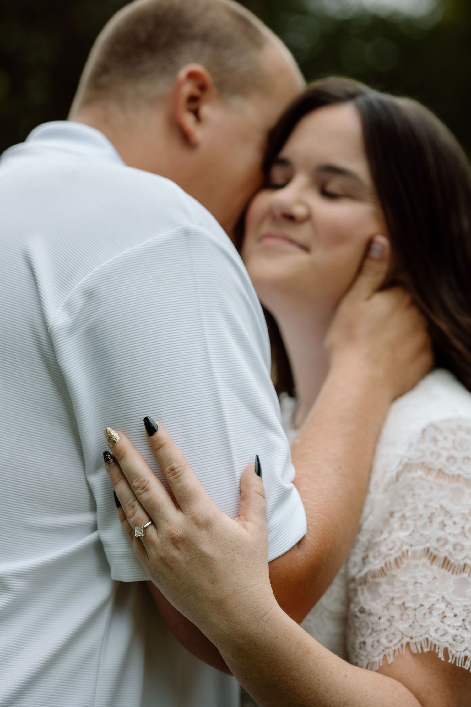 Couple sharing a tender moment, woman smiling with eyes closed wearing engagement ring and black nails.