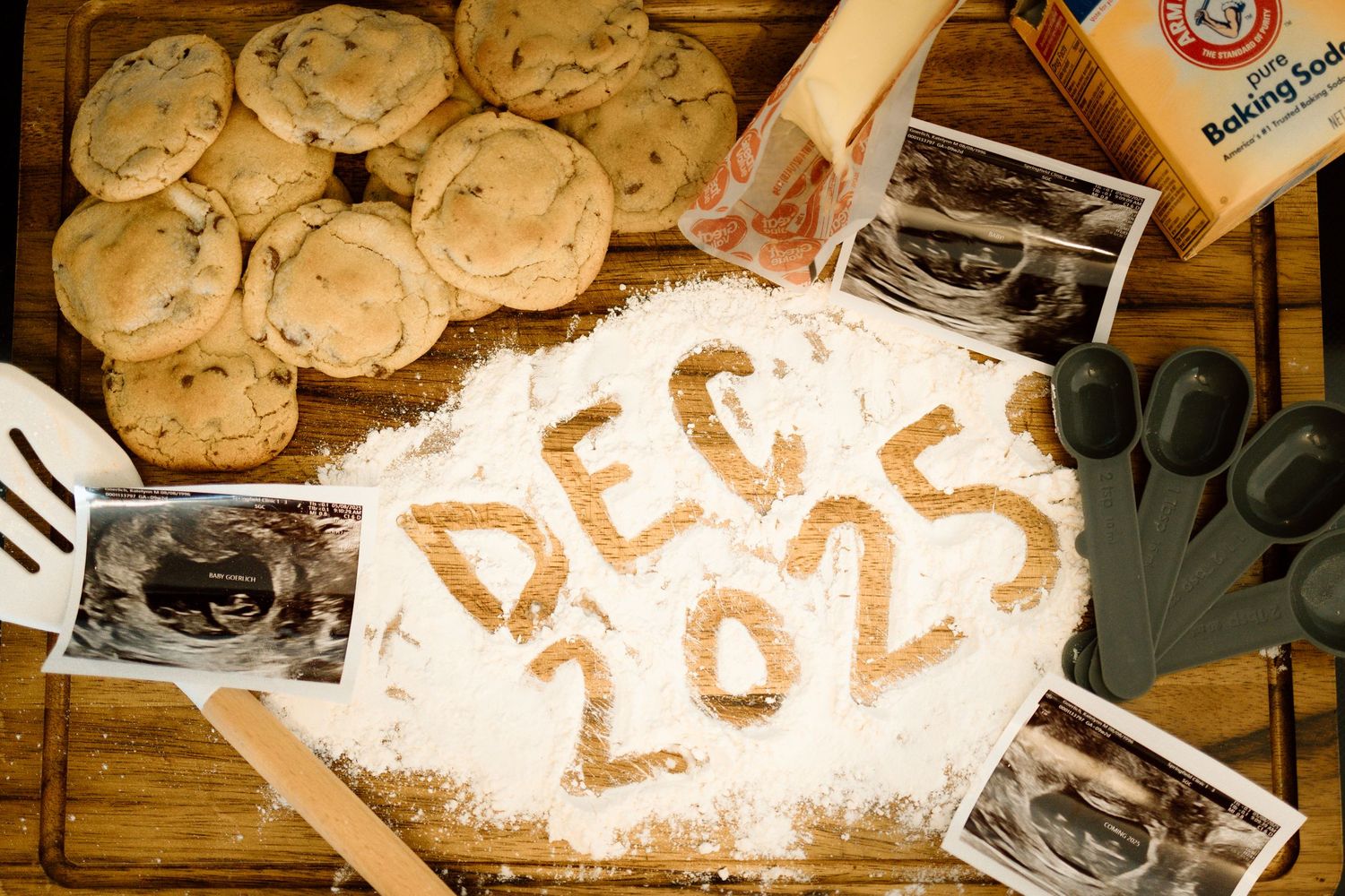 Pregnancy announcement with Dec 2025 written in flour surrounded by cookies and ultrasound photos.