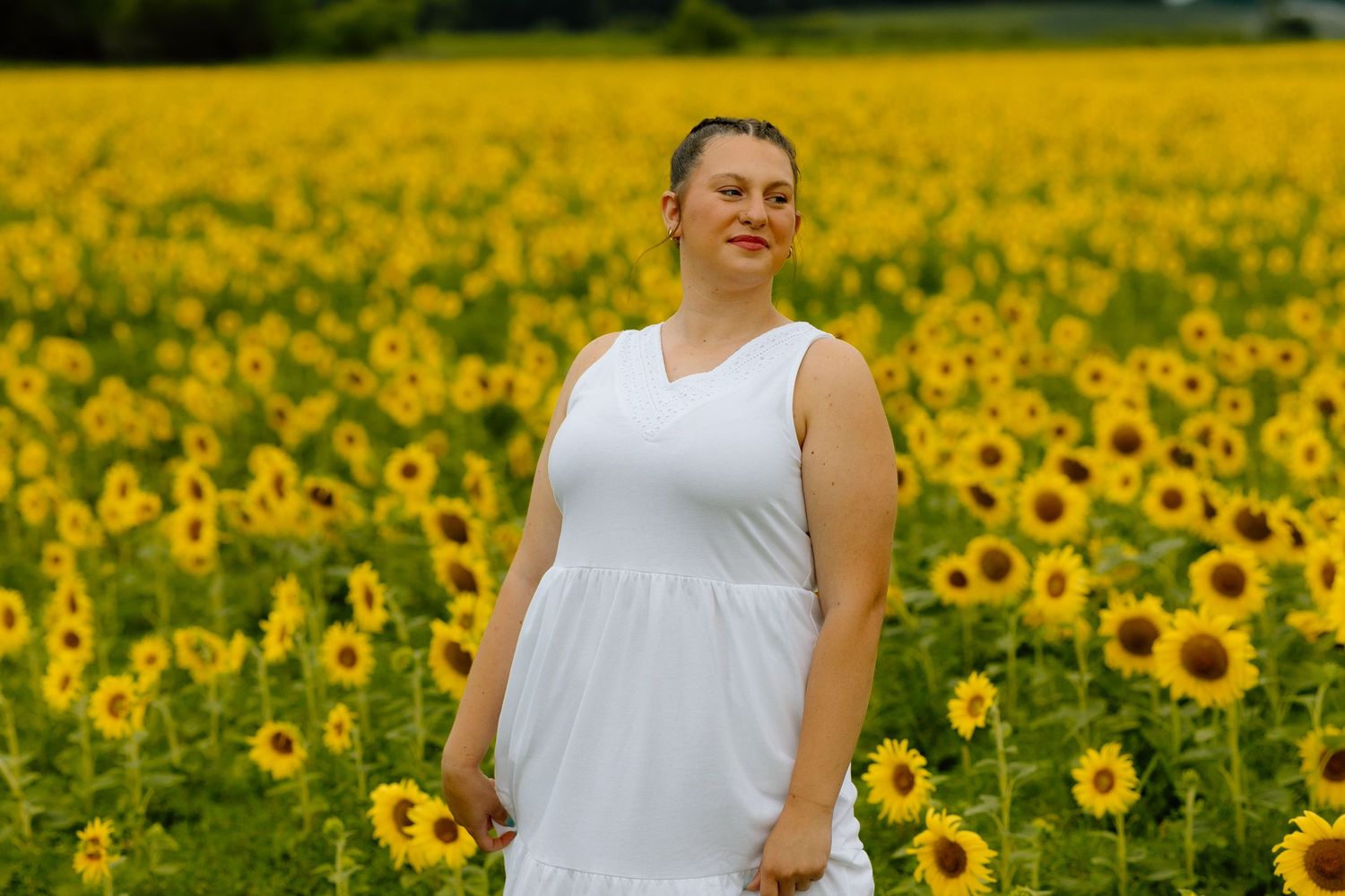 Happy woman in white sleeveless dress posing in a bright yellow sunflower field outdoors.