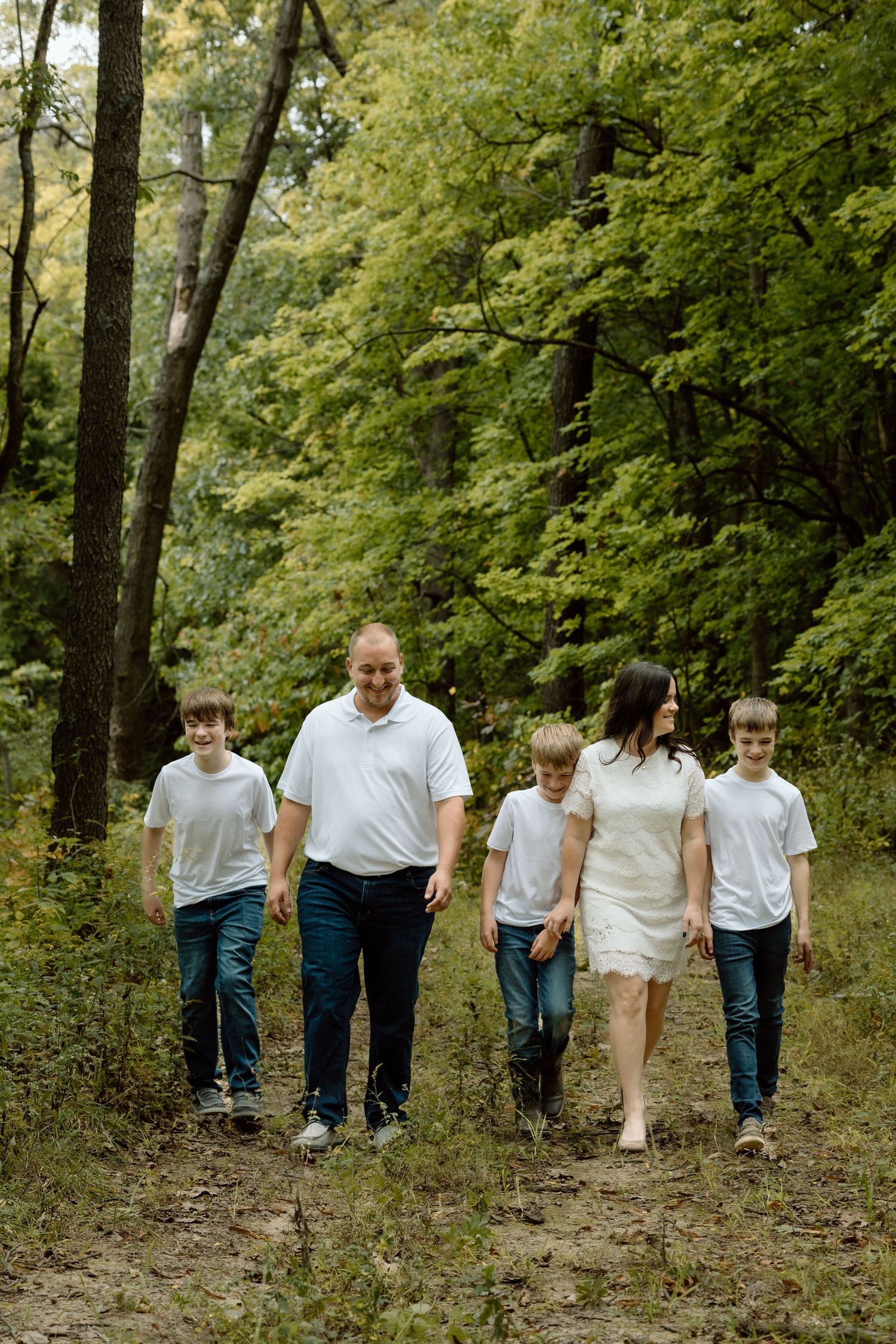 Family of five in white shirts and jeans walking together on a wooded forest trail.