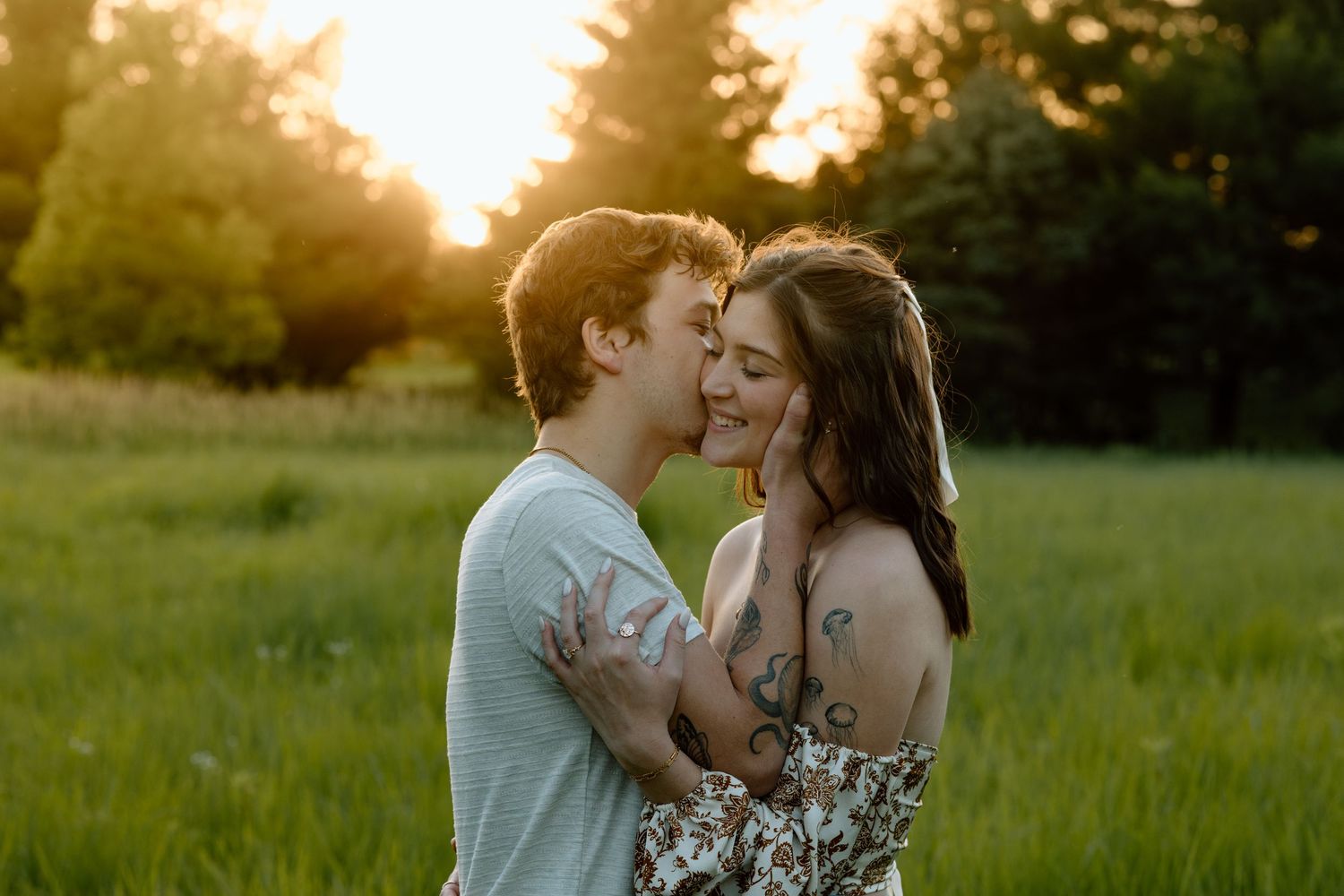 Couple nearly kissing in a sunlit green meadow during a beautiful golden sunset.