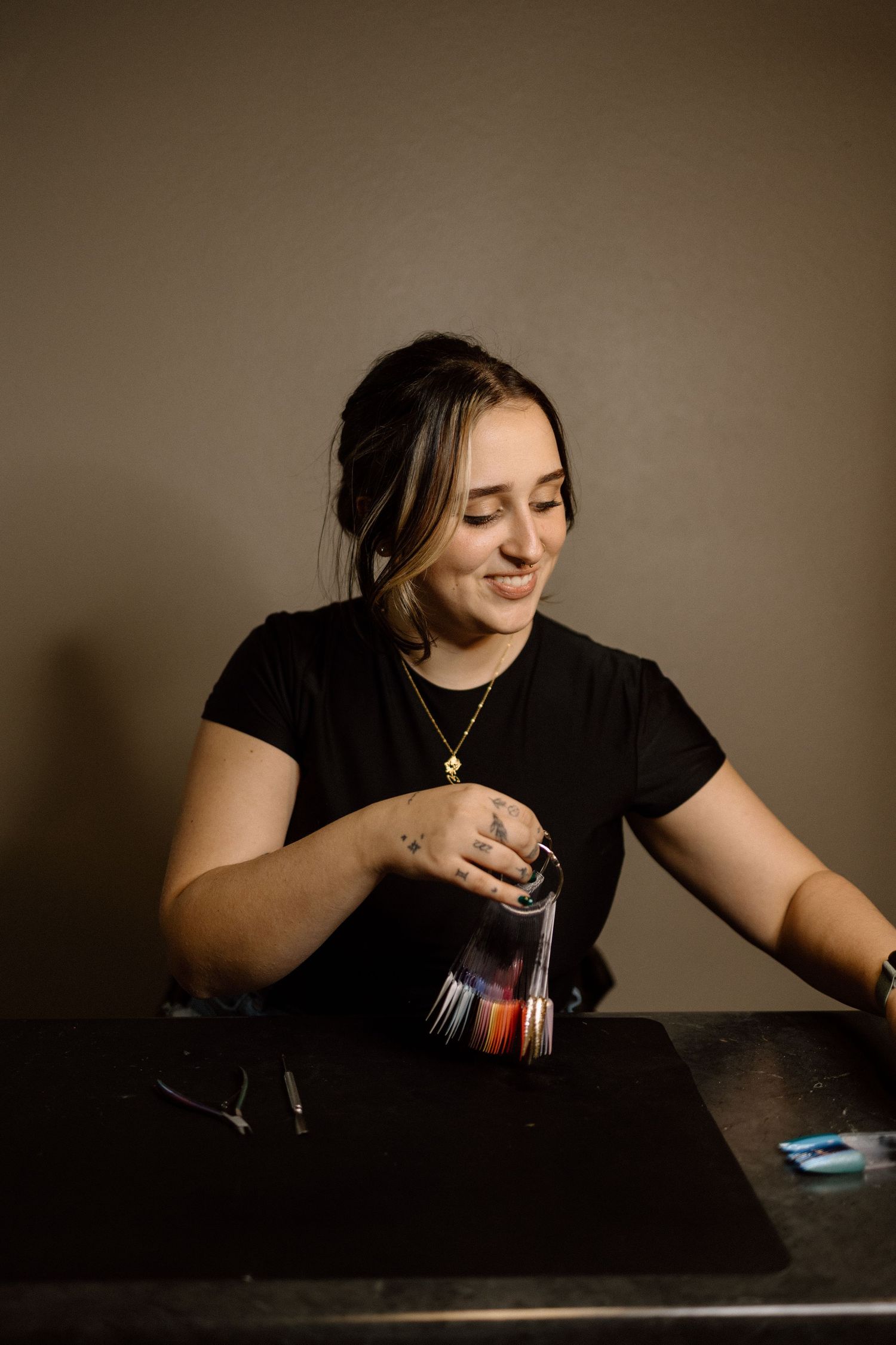 A young woman in black smiles while holding a fan of nail color swatches at a table.