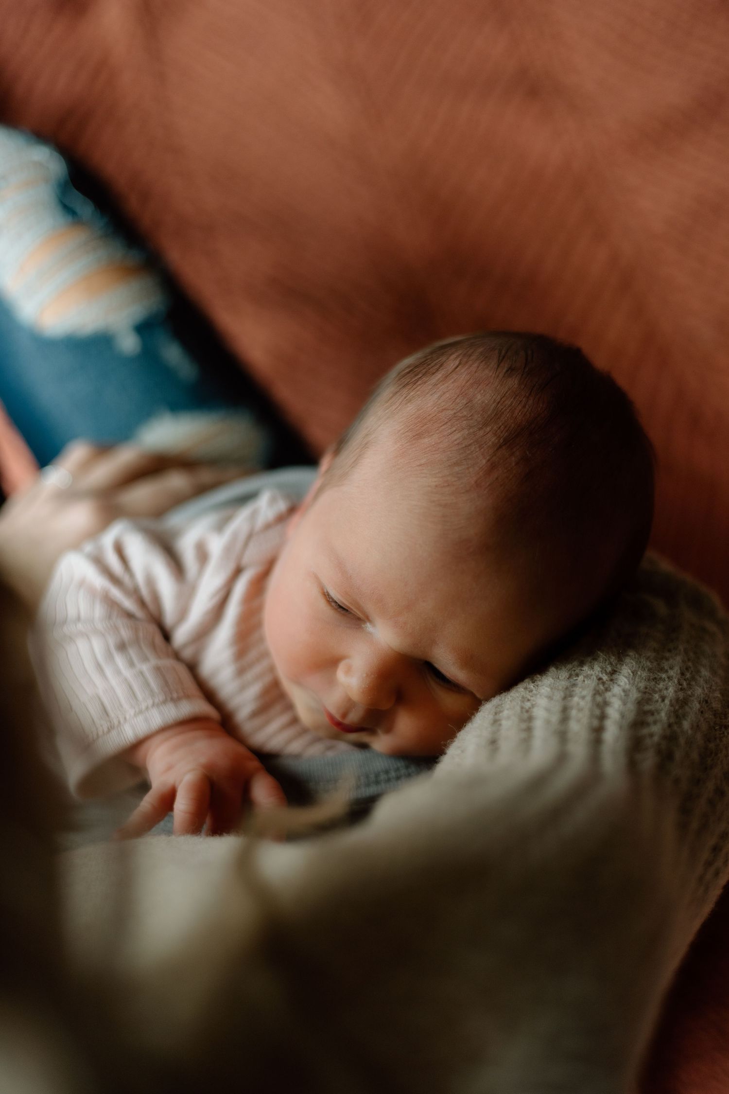 Peaceful sleeping newborn baby in pink knit onesie resting on a soft gray blanket.