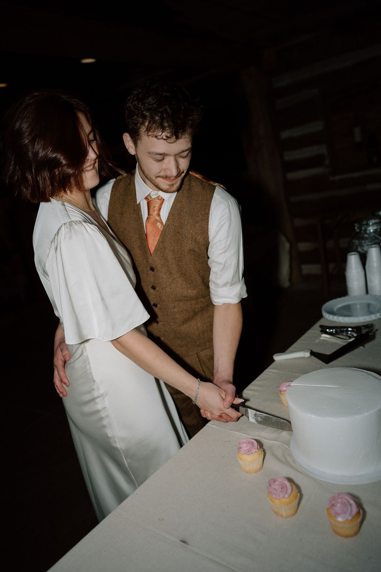 Bride and groom cut wedding cake together at rustic barn reception.