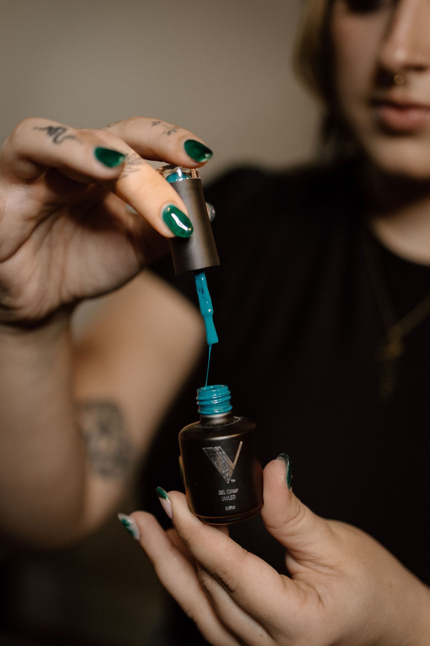 Person with green nail polish applying teal gel nail polish from a dark bottle.