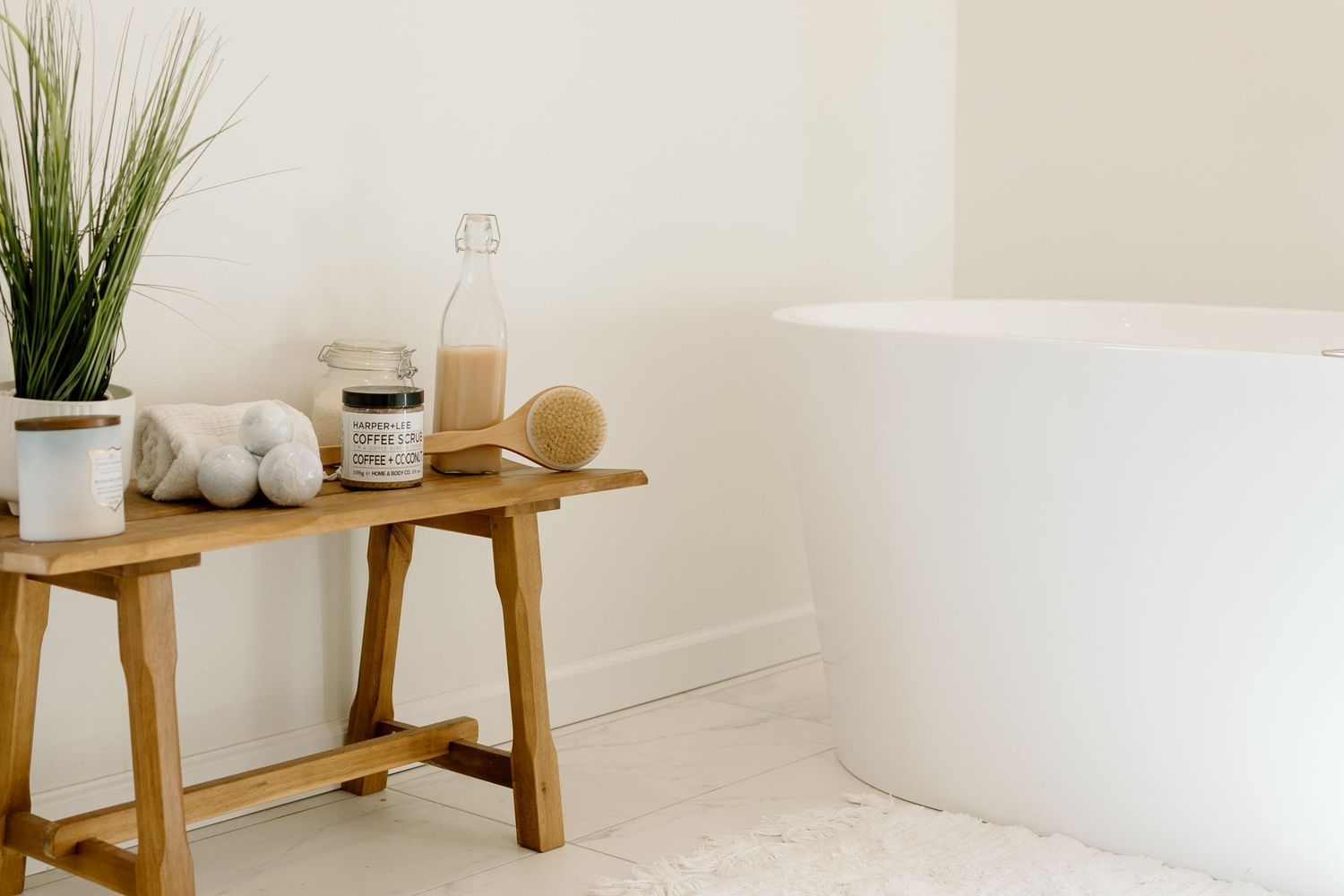 Minimalist white bathroom with freestanding tub and wooden stool with spa products.