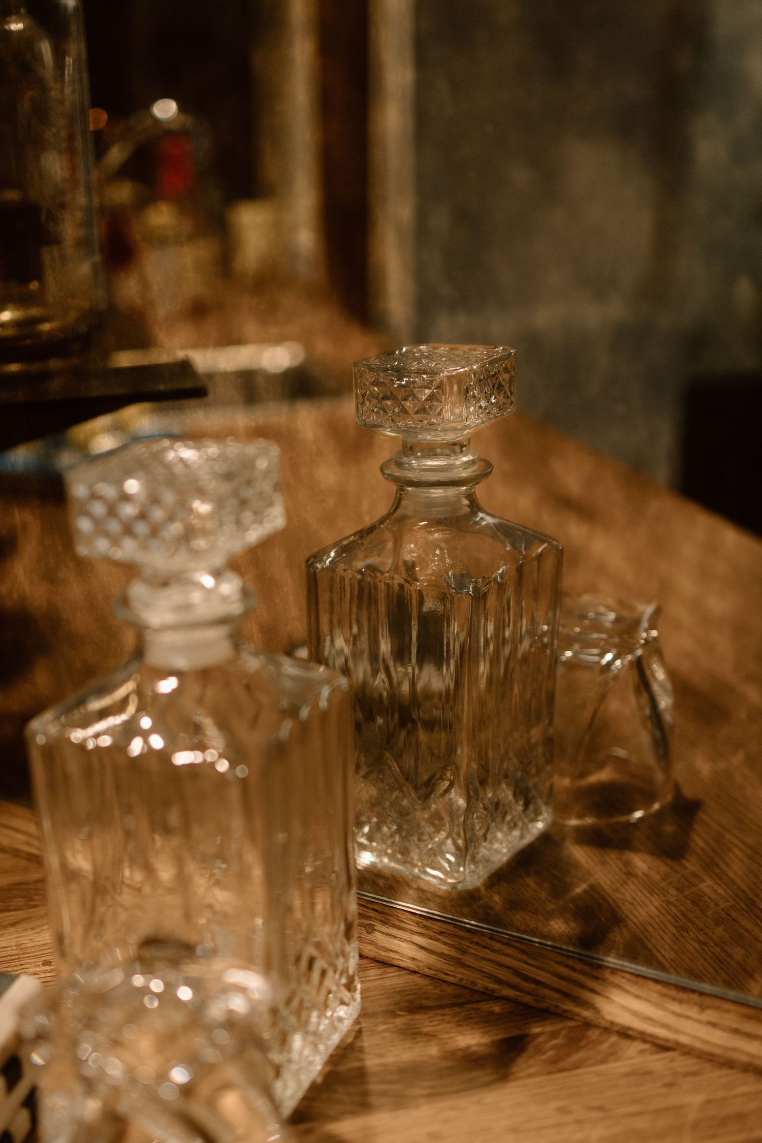 Two ornate crystal whiskey decanters with stoppers on a wooden surface in warm moody lighting.