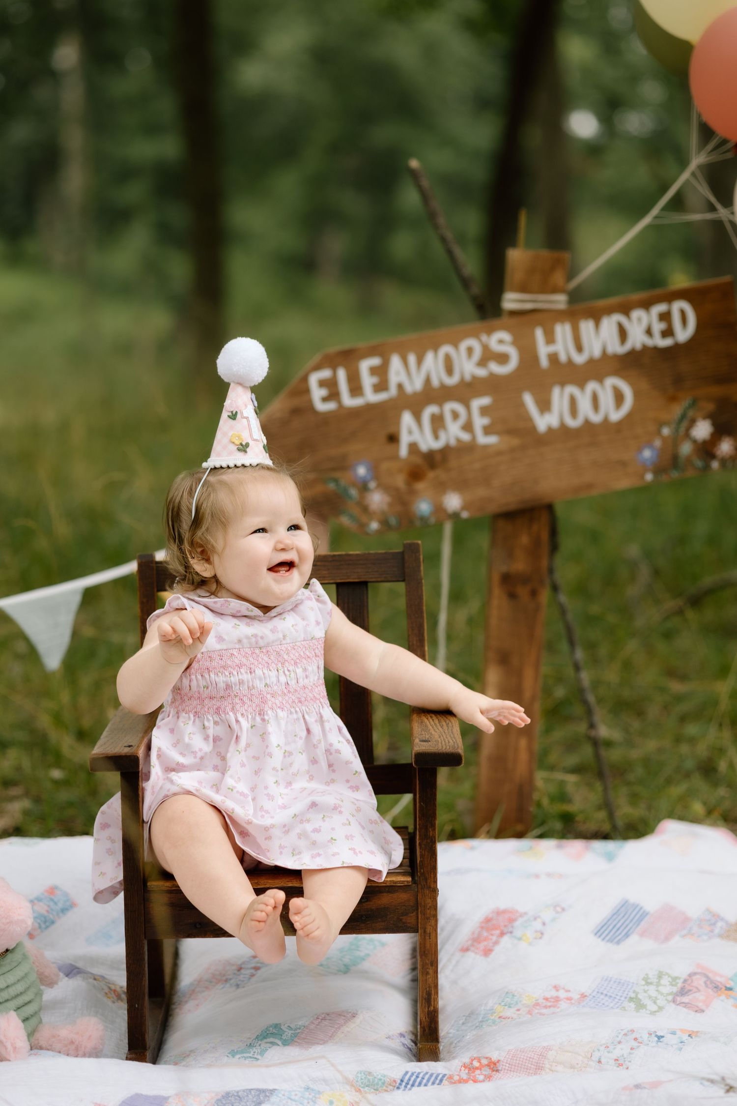 Happy baby girl celebrating first birthday in floral dress at Hundred Acre Wood party.