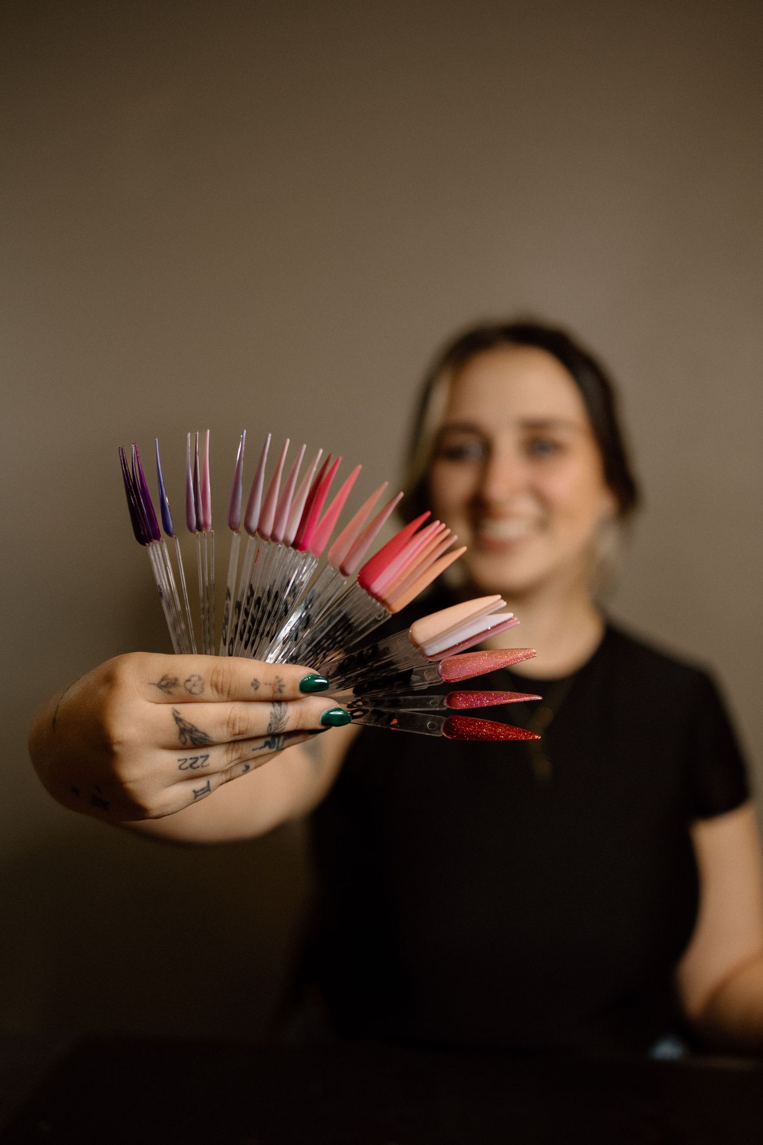 A smiling nail technician holds up a colorful fan of nail polish sample tips toward camera.