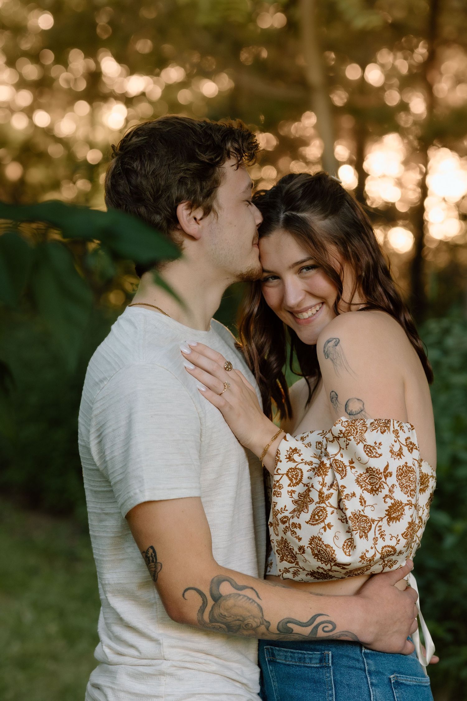 Man kissing smiling woman on cheek during golden hour in a forest setting.