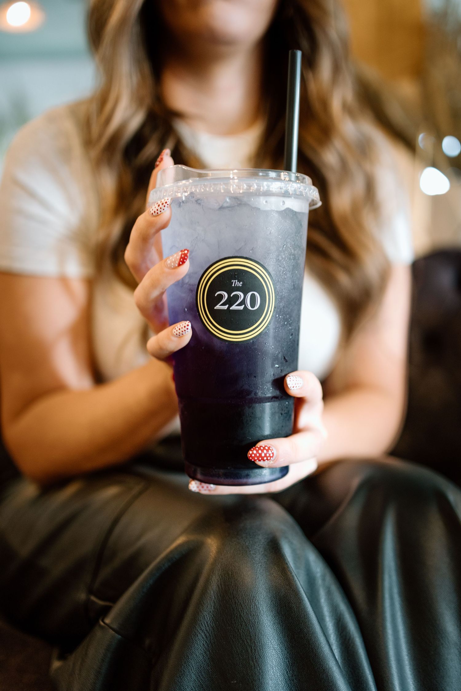 Woman with red nail art holding large iced purple drink in The 220 branded cup.