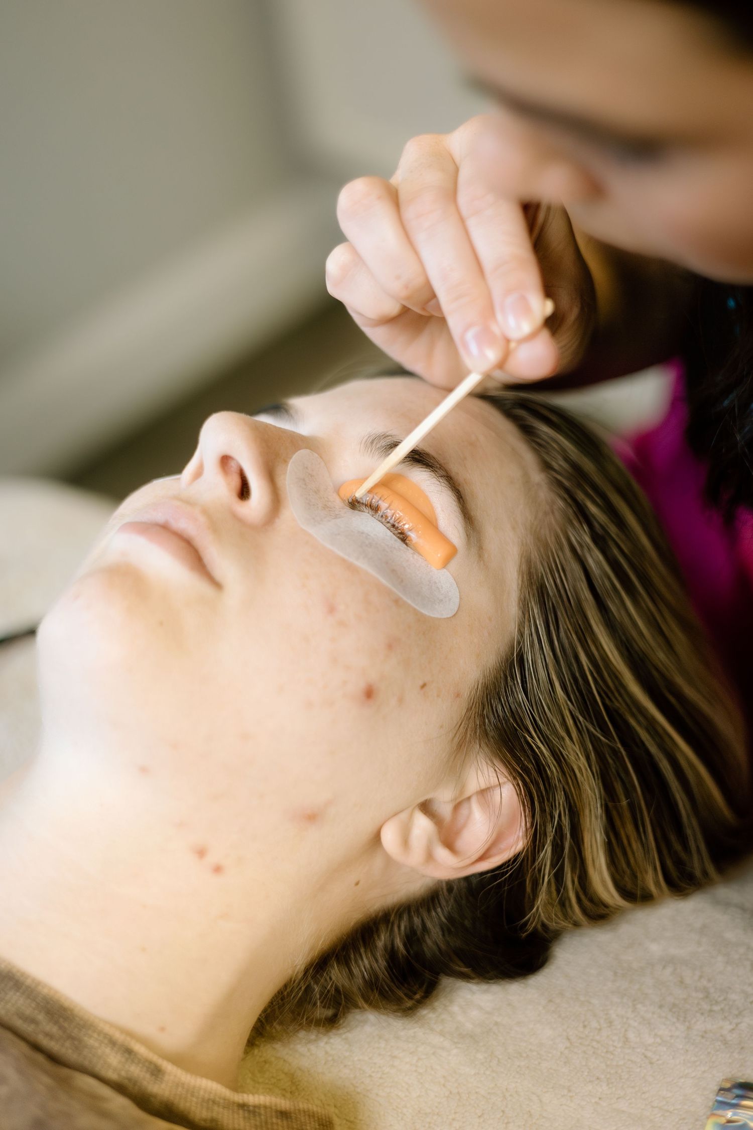 Close-up of lash lift treatment being applied to young woman with eye pads in a beauty salon.