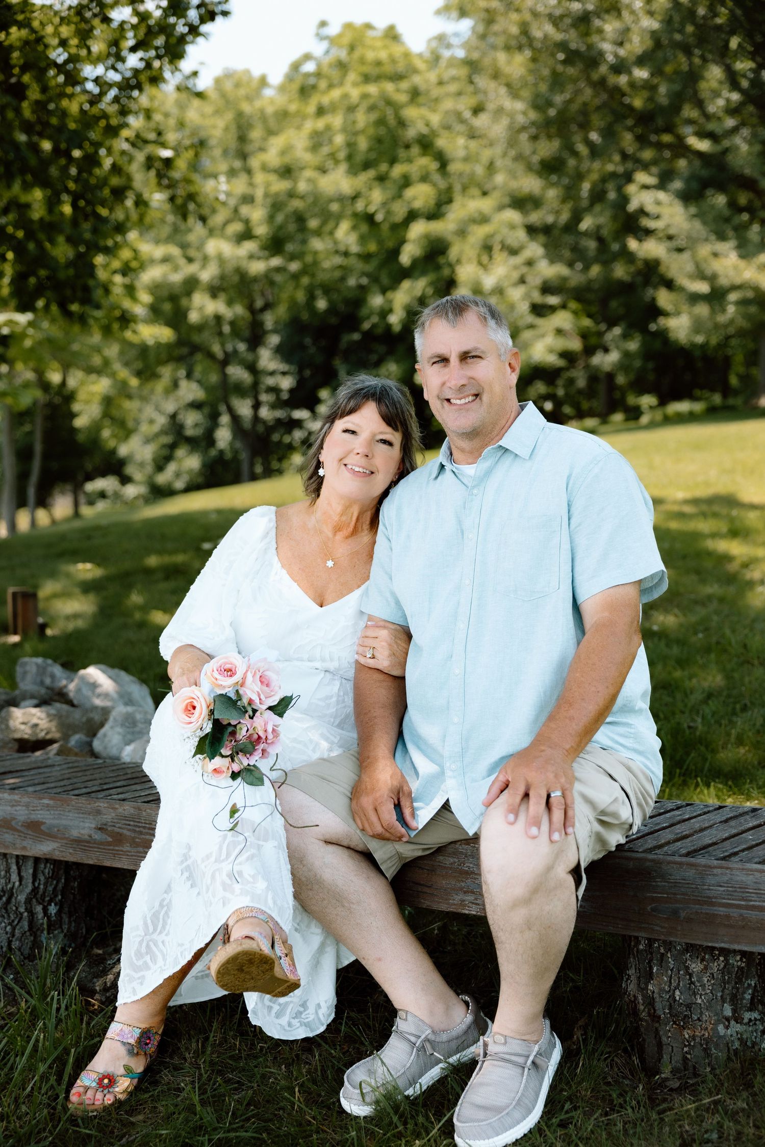 Smiling middle-aged couple sitting on a wooden bench in a lush green park.