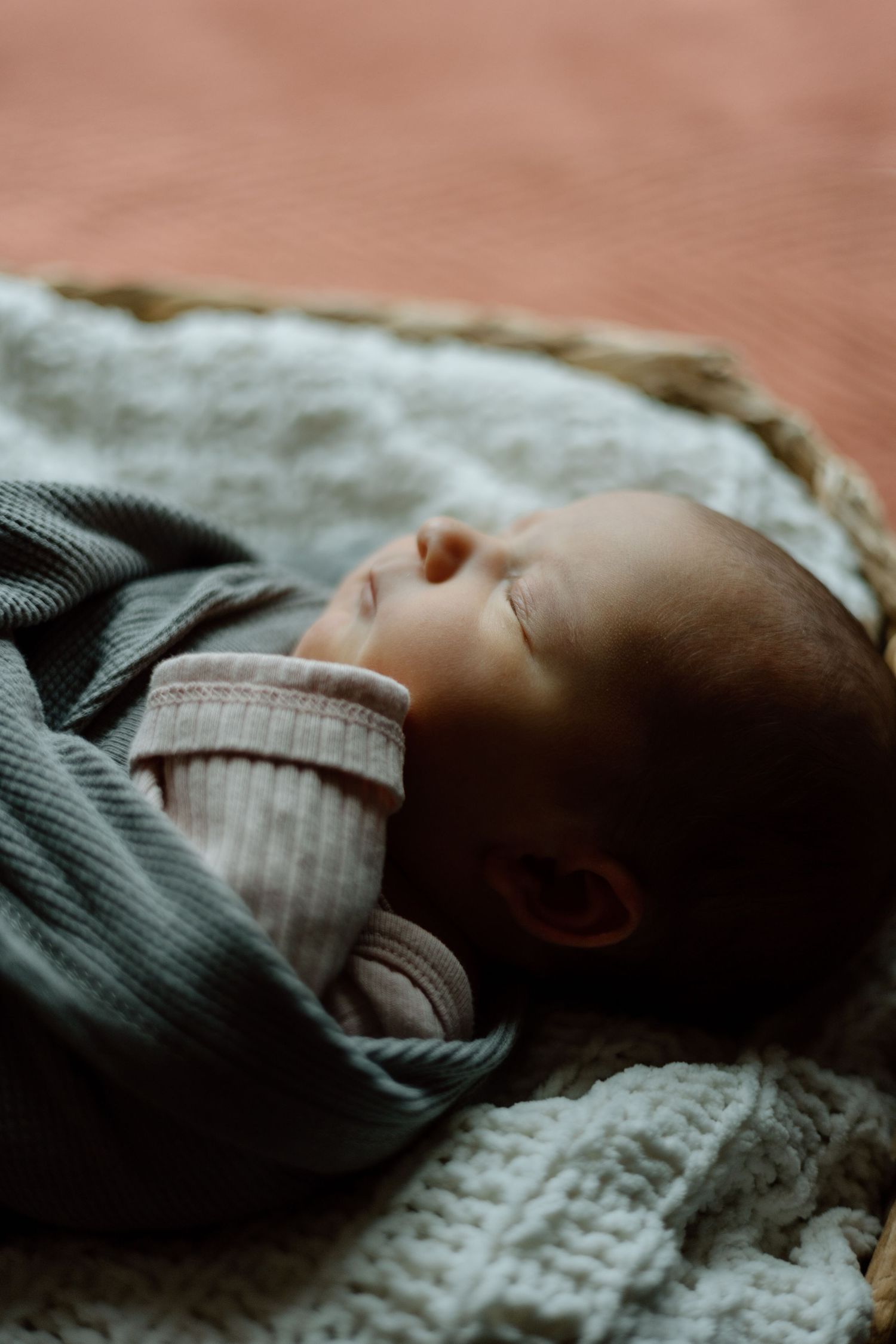 Close-up of sleeping newborn baby wrapped in gray swaddle blanket in a wicker basket.