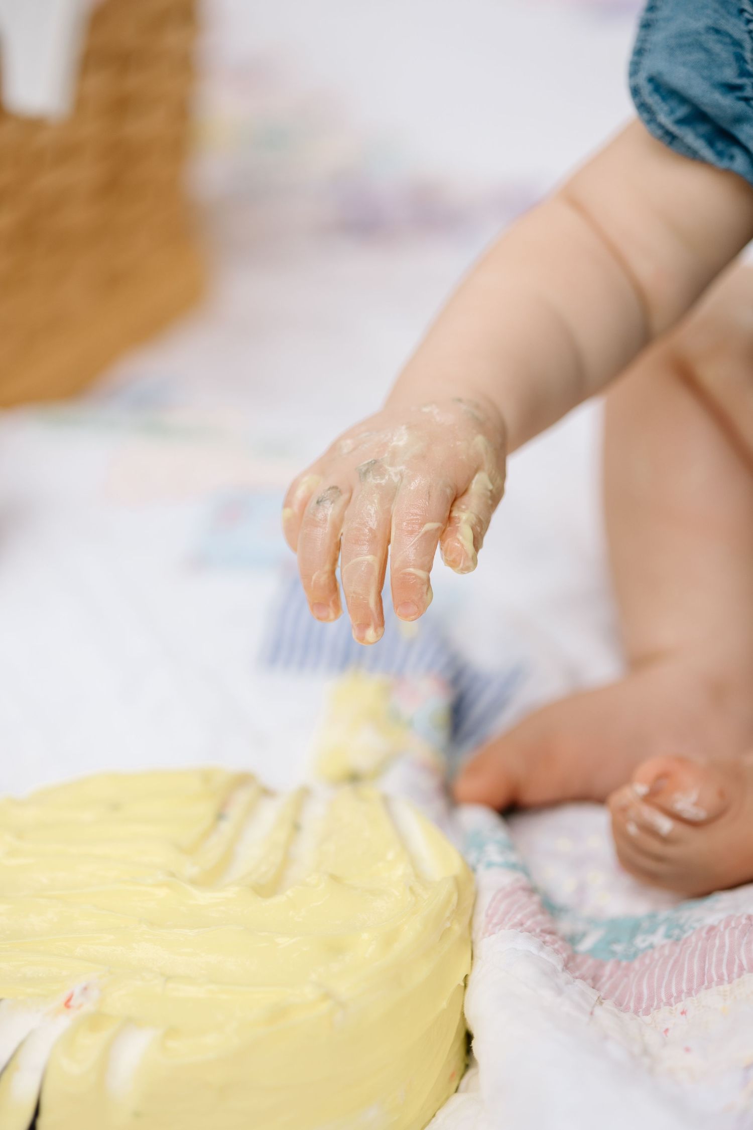 Close-up of baby hands covered in yellow frosting from first birthday smash cake on quilt.