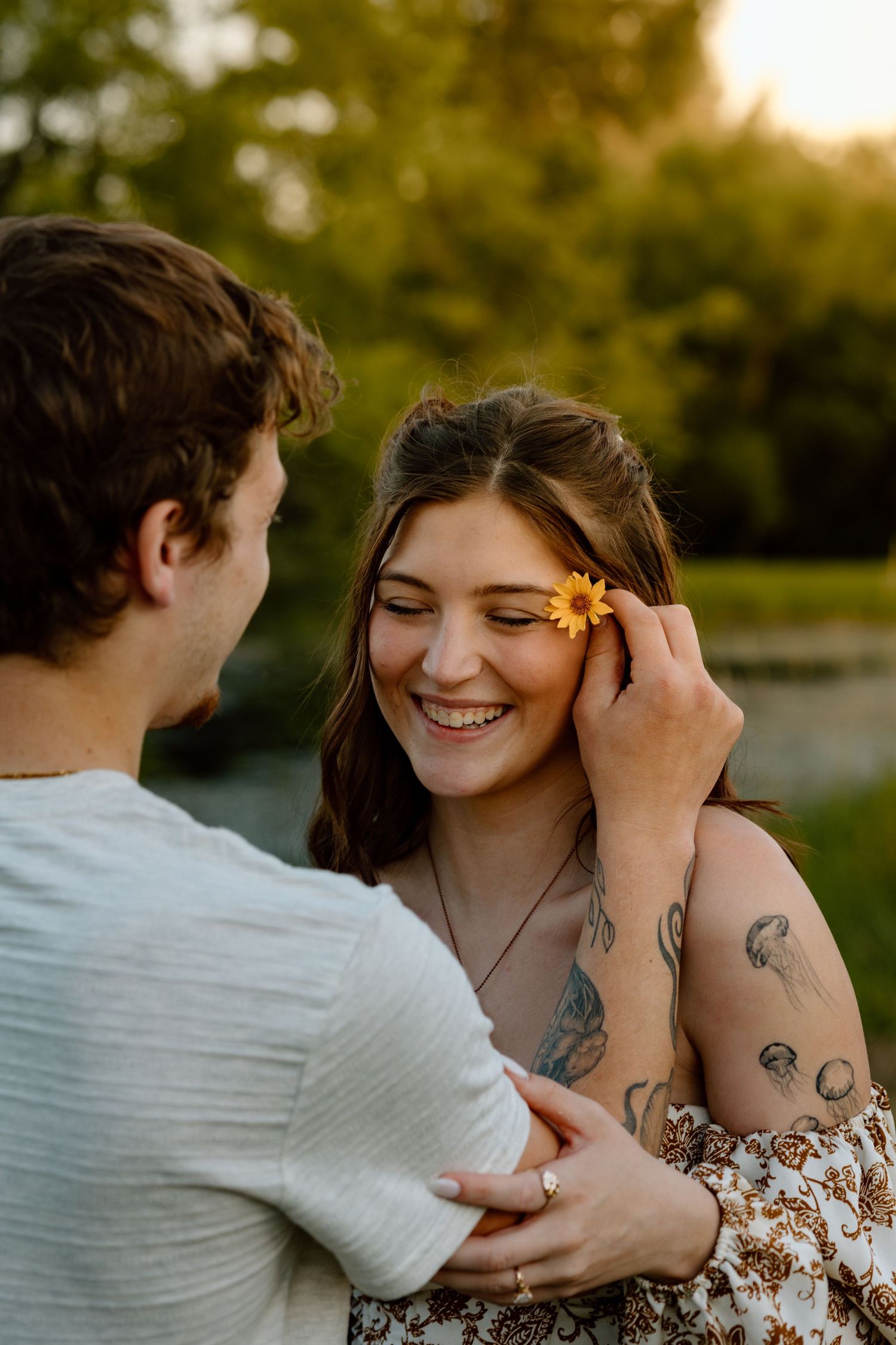 Man placing a yellow flower in smiling woman's hair during golden hour outdoors.