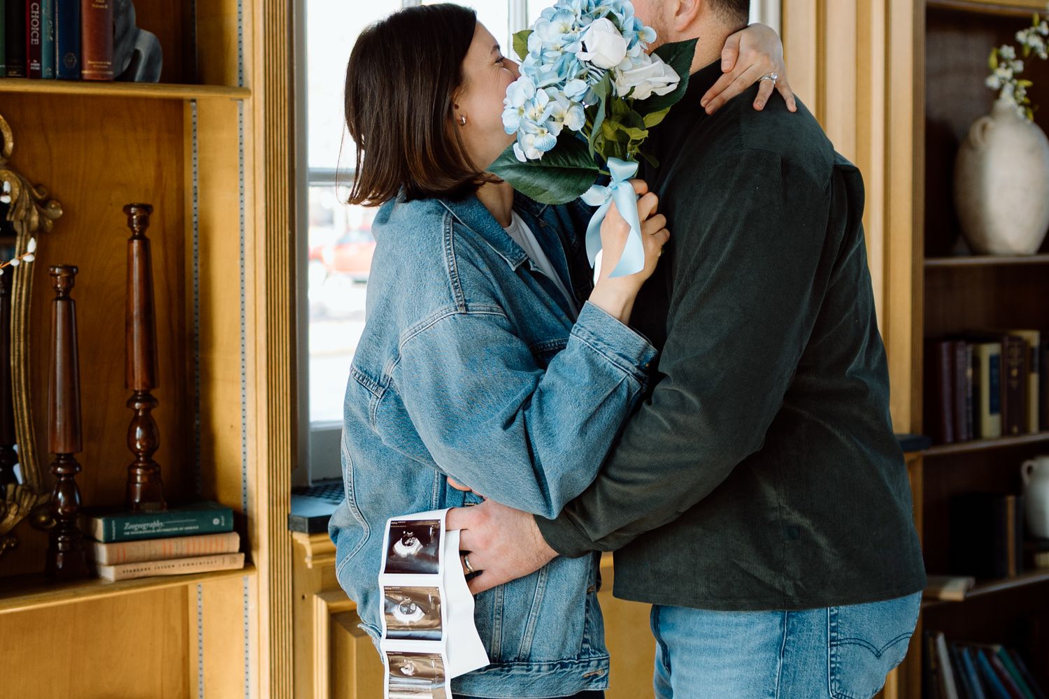 Couple shares romantic moment with blue flowers and ultrasound photos during pregnancy announcement.